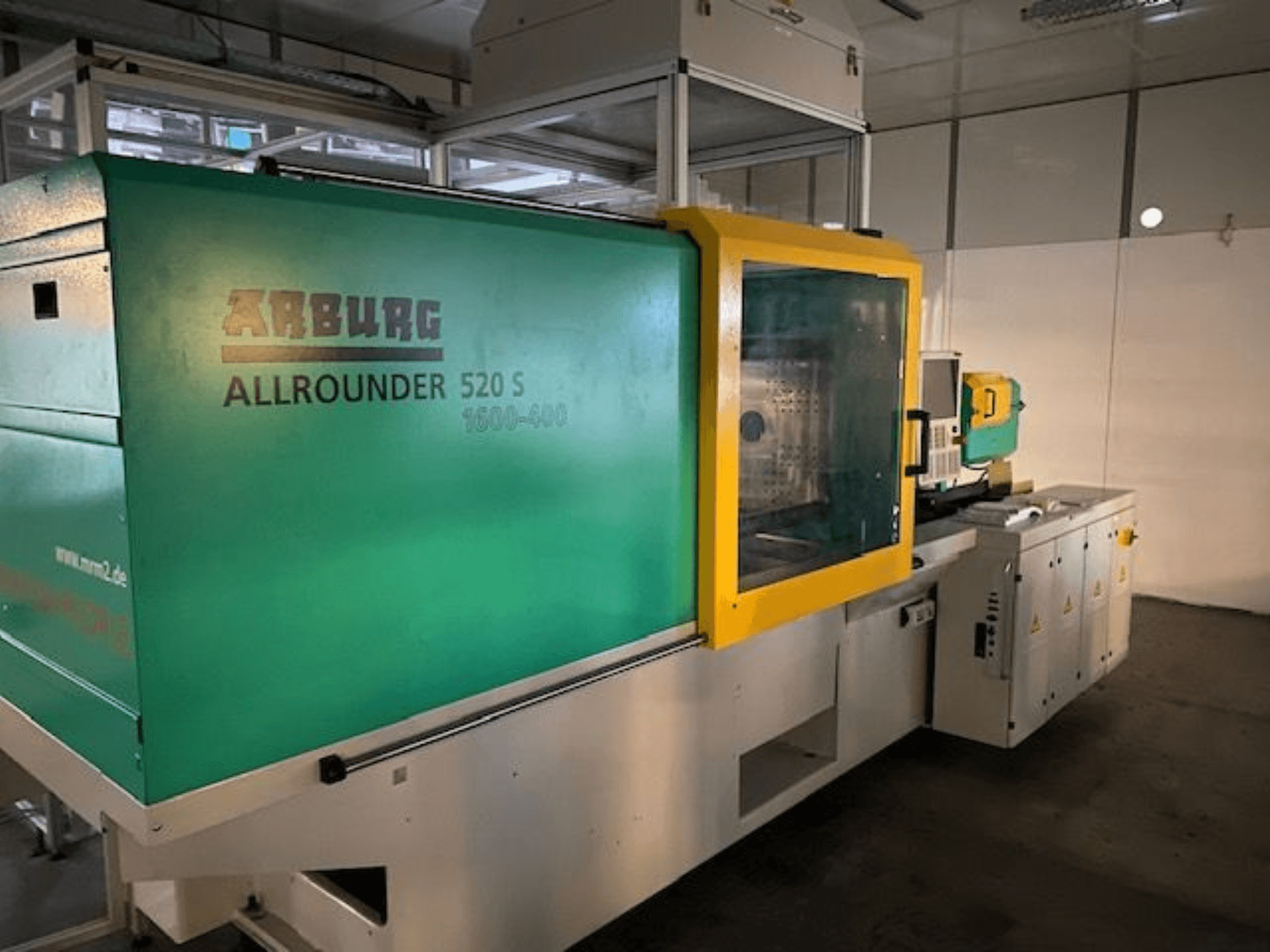 Žalios ir geltonos spalvos šoninis vaizdas, matomos techninės detalės, "Arburg Allrounder 520 S" įpurškimo liejimo mašina.