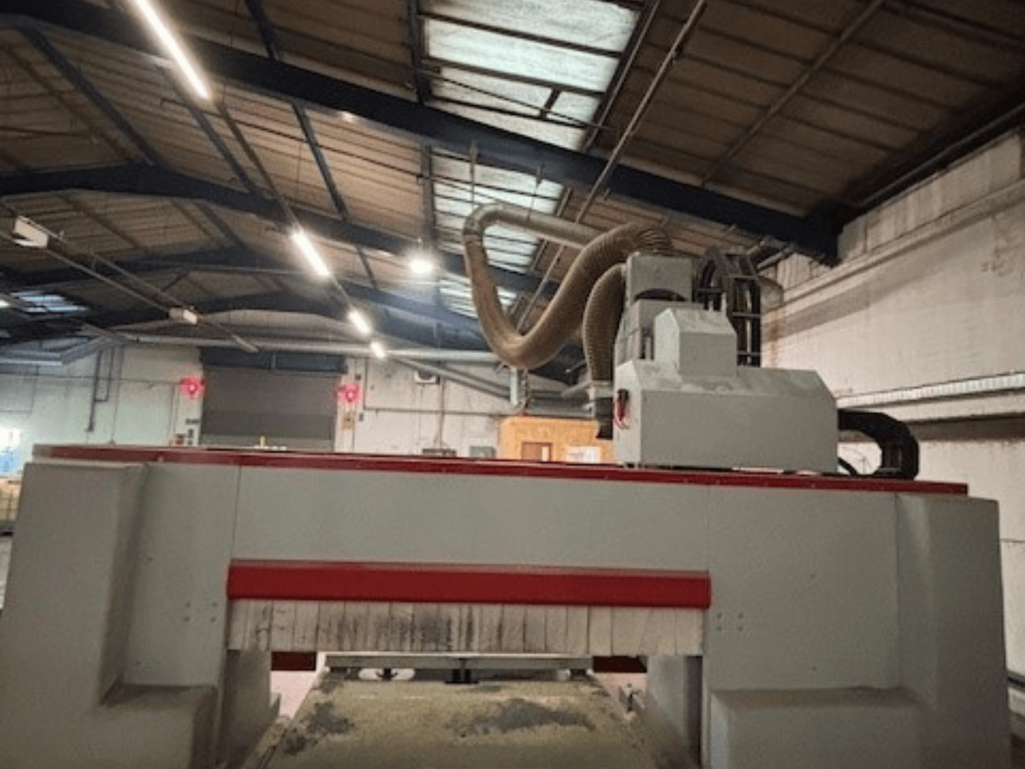 CNC frezavimo staklės dirbtuvėse, šoninis vaizdas, išryškinantis raudoną ir pilką dizainą, pritvirtinta dulkių ištraukimo sistema.