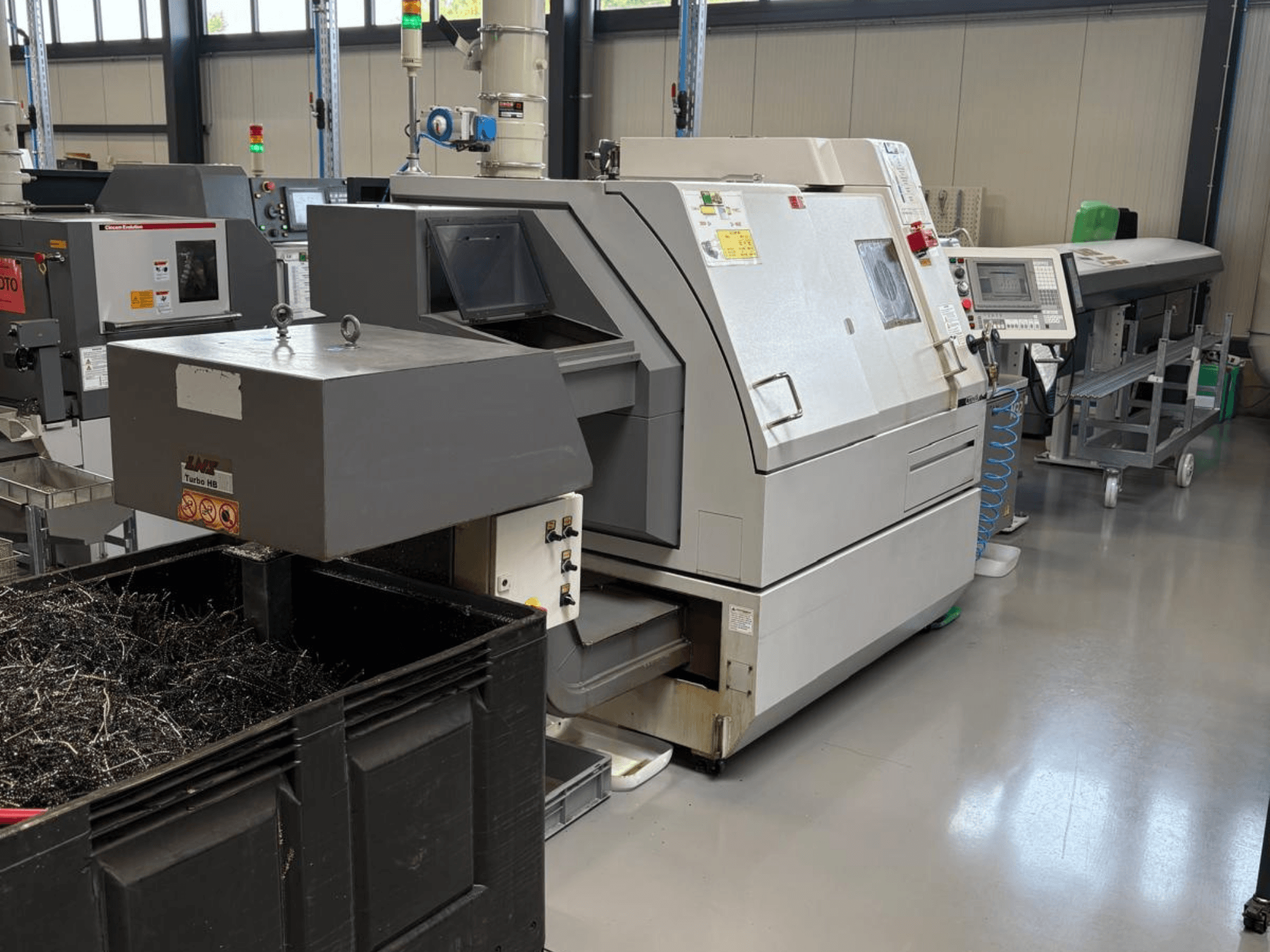 Pramoninė mašina LTA Turbo H8, vaizdas iš šono, su dideliu metalo drožlių konteineriu ir valdymo skydeliu gamykloje.