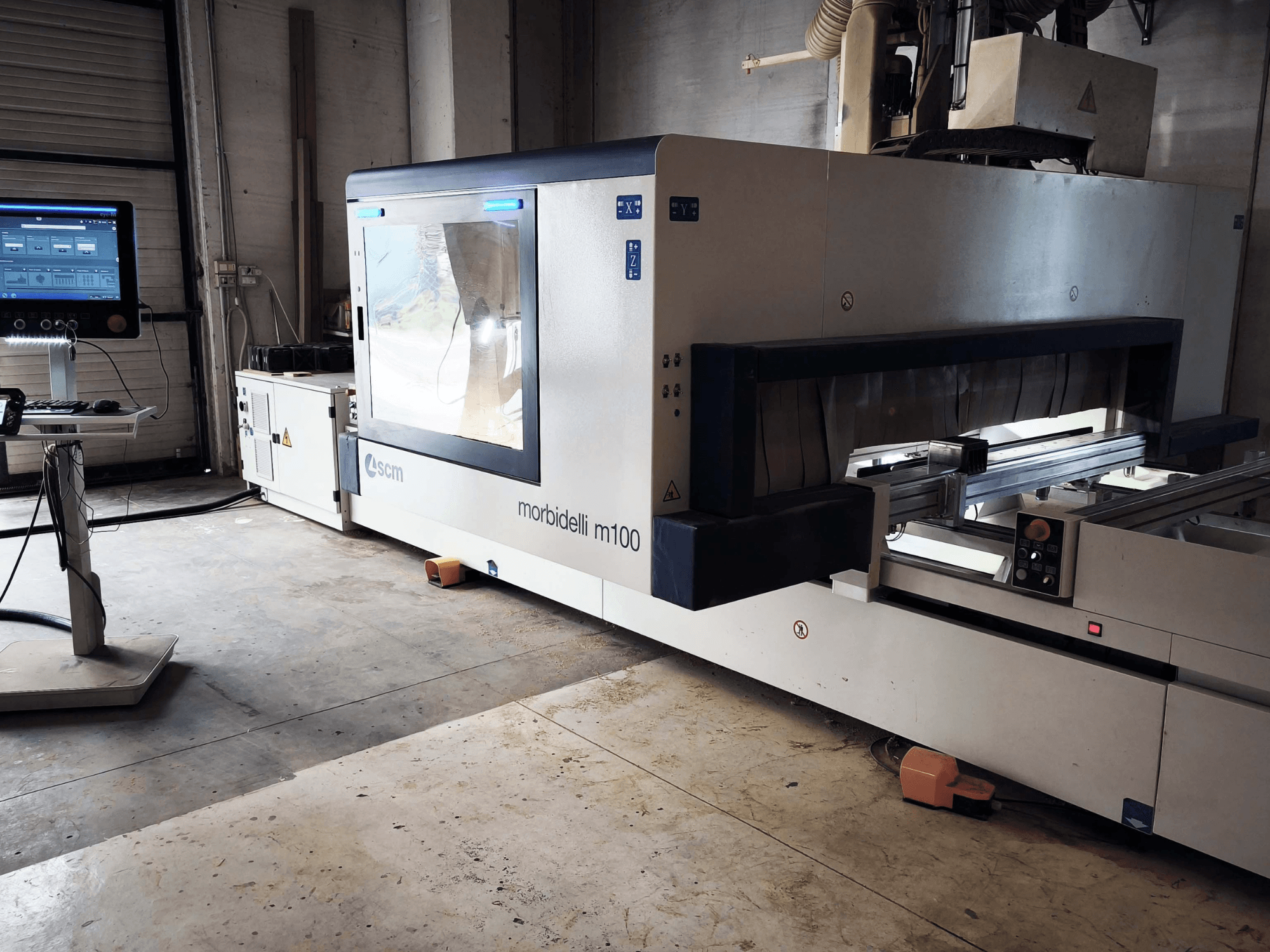 SCM „Morbidelli M 100“ CNC medžio apdirbimo centras, vaizdas iš šono, kuriame matomas valdymo pultas, darbo zona ir saugos elementai.