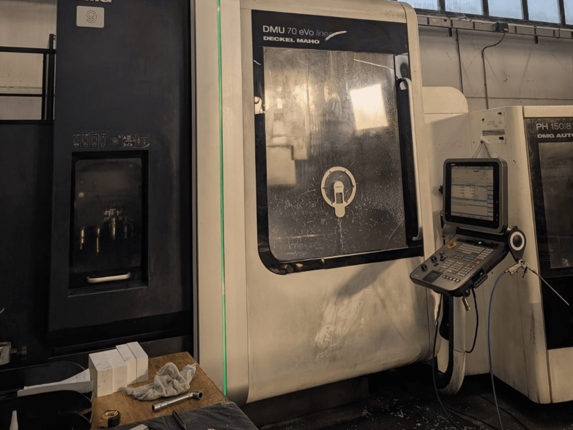 DMG DECKEL MAHO DMU 70 EVO Linijinis vertikalusis apdirbimo centras, vaizdas iš priekio, matomas valdymo skydelis, įrankiai ir darbo vieta.