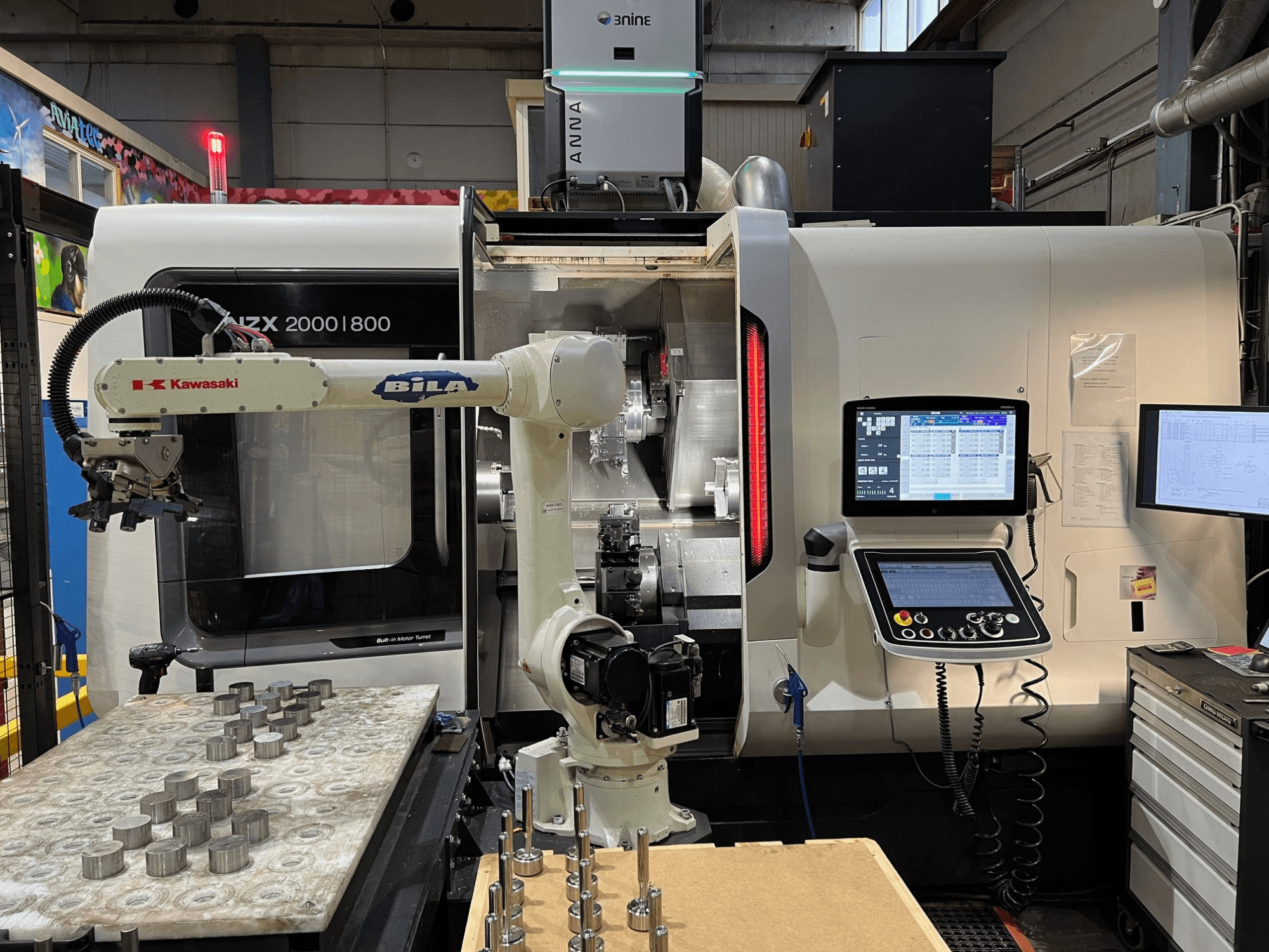 Gamybos ceche esanti horizontali tekinimo staklė „DMG MORI NZX 2000/800SY“, kurioje matoma „Kawasaki“ robotinė ranka ir valdymo pultas.