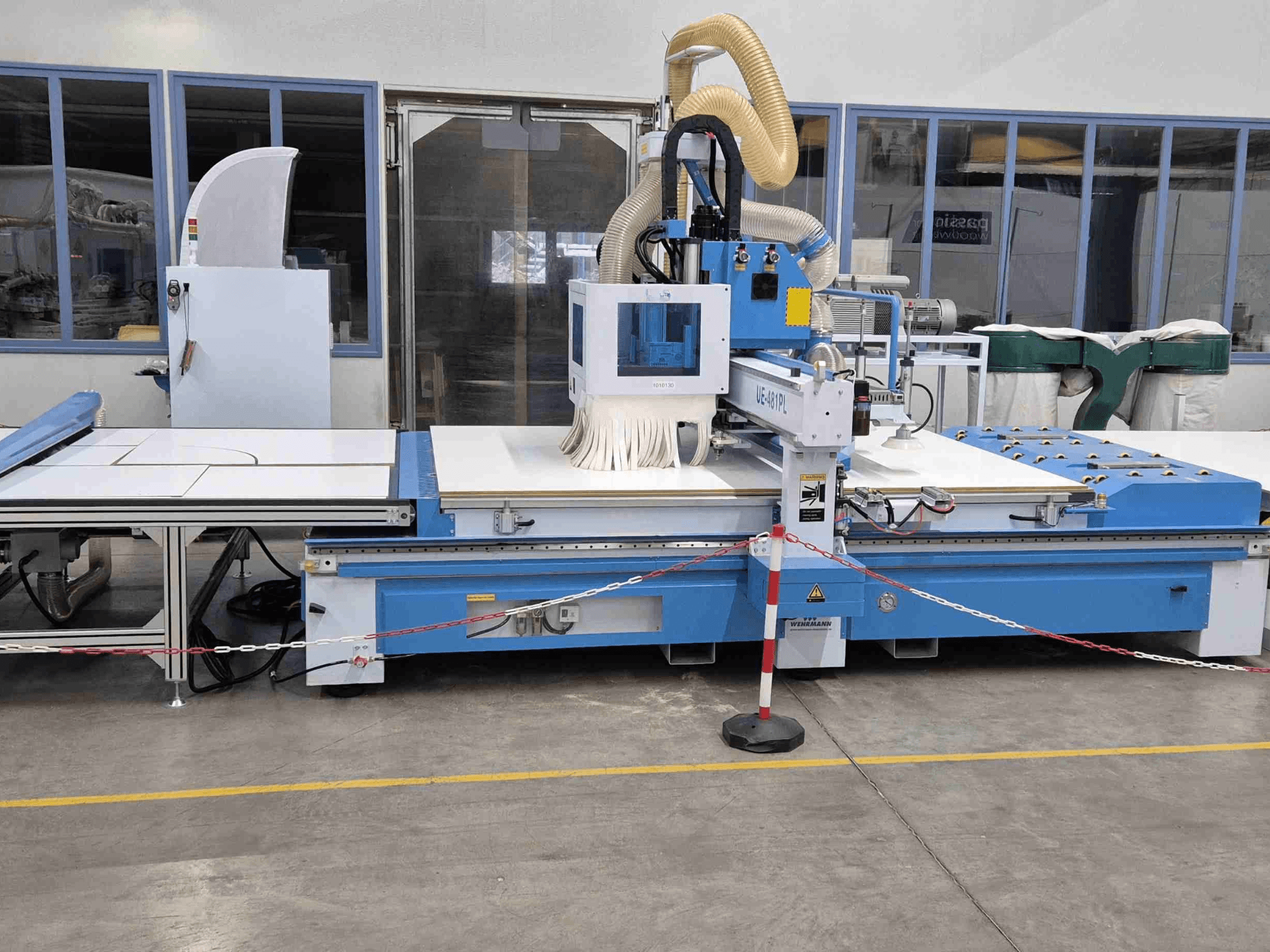 Mėlynasis CNC maršrutizatorius UE-621PL iš priekio su dideliu pjovimo stalu ir prijungta dulkių nusiurbimo sistema.