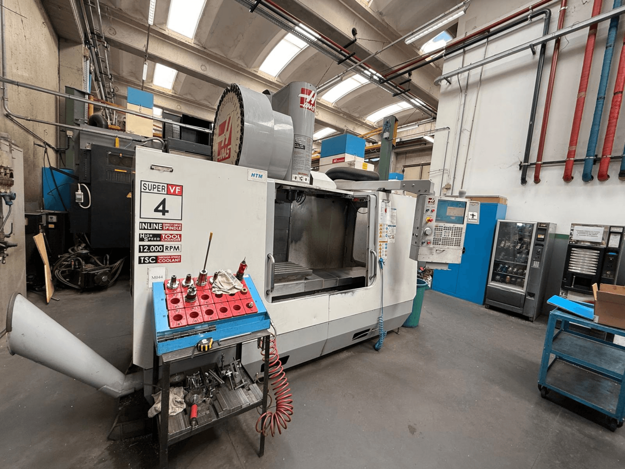 HAAS Super VF 4 CNC frezavimo staklės su valdymo pultu, 12 000 aps/min sukliu ir įrankiais ant mėlyno laikiklio, vaizdas iš šono.