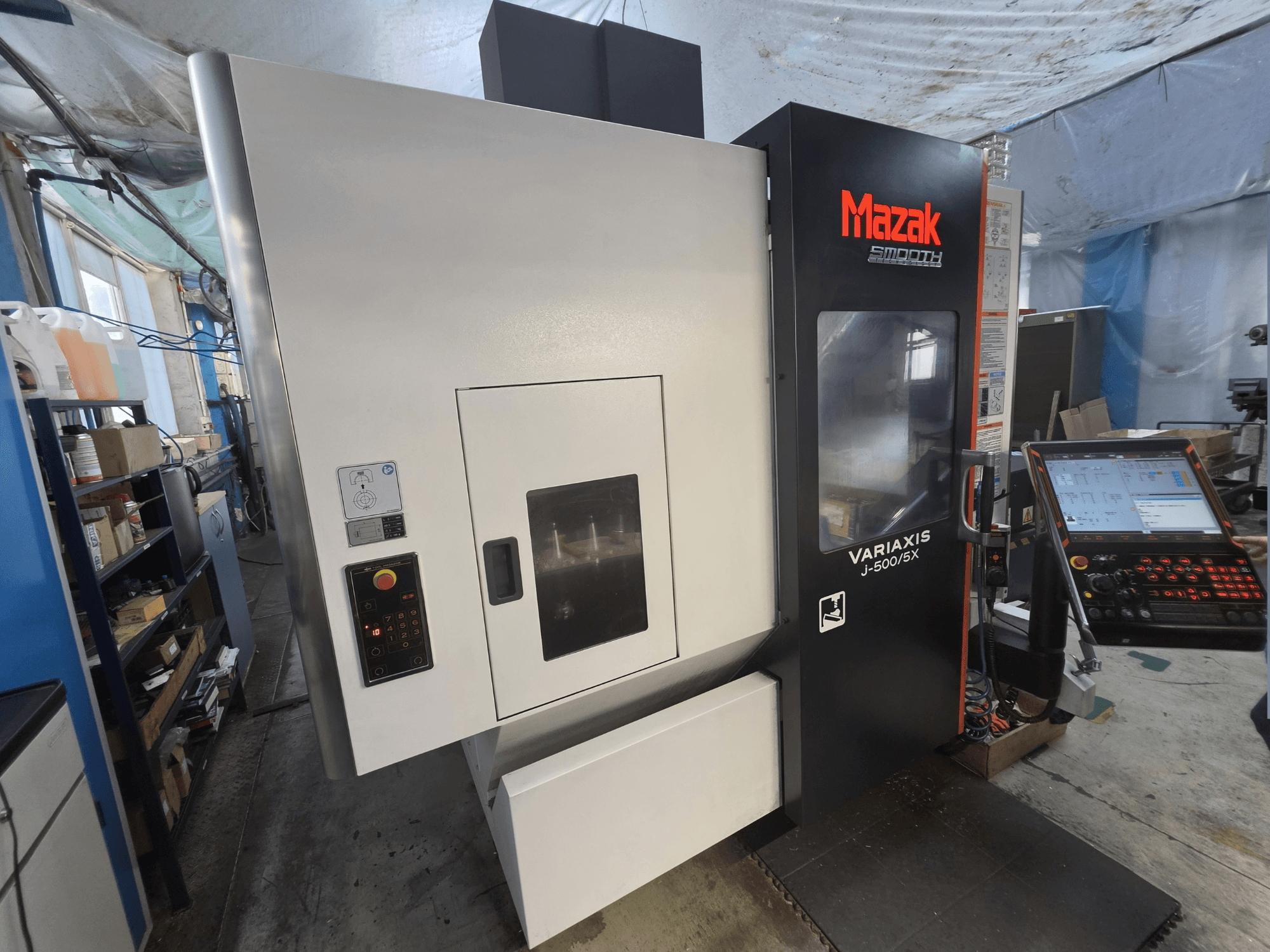„Mazak VARIAXIS J-500/5X“ vertikalus apdirbimo centras, vaizdas iš priekio, su valdymo pultu ir dideliu apdirbimo langu.