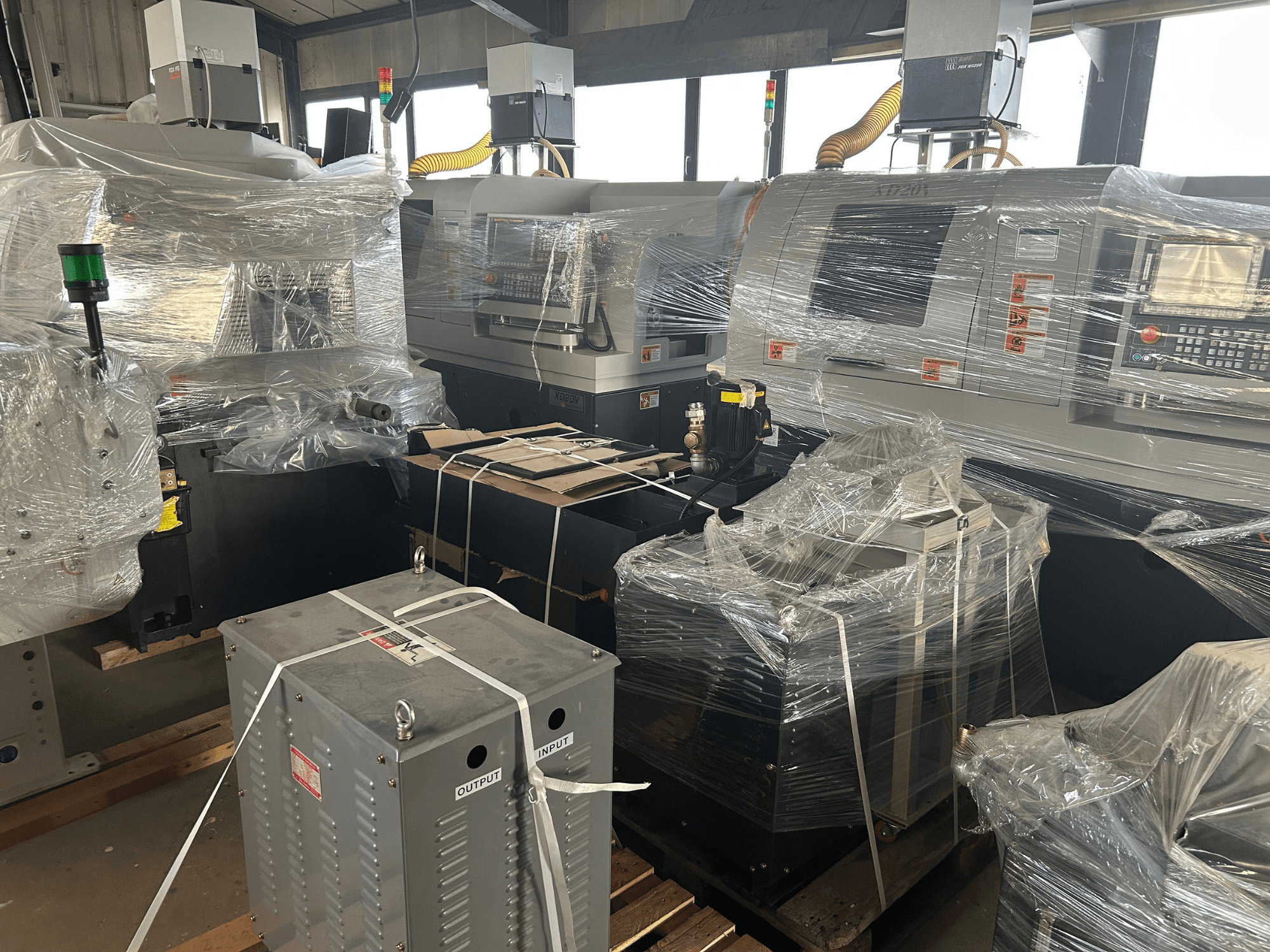 "Hanwha XD20" šveicariško tipo tekinimo staklės, vaizdas iš priekio, apvyniotos plastiku, matomas valdymo skydelis ir priedai sandėlyje.