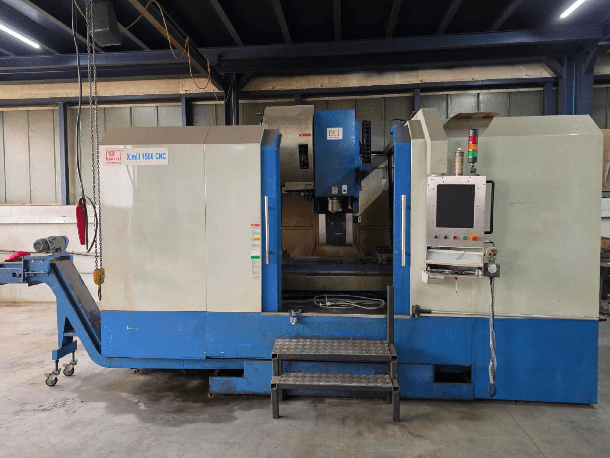 CNC vertikalusis apdirbimo centras „KNUTH X-MILL 1500“, vaizdas iš šono; matyti valdymo pultas, laipteliai ir išvežimo konvejeris.