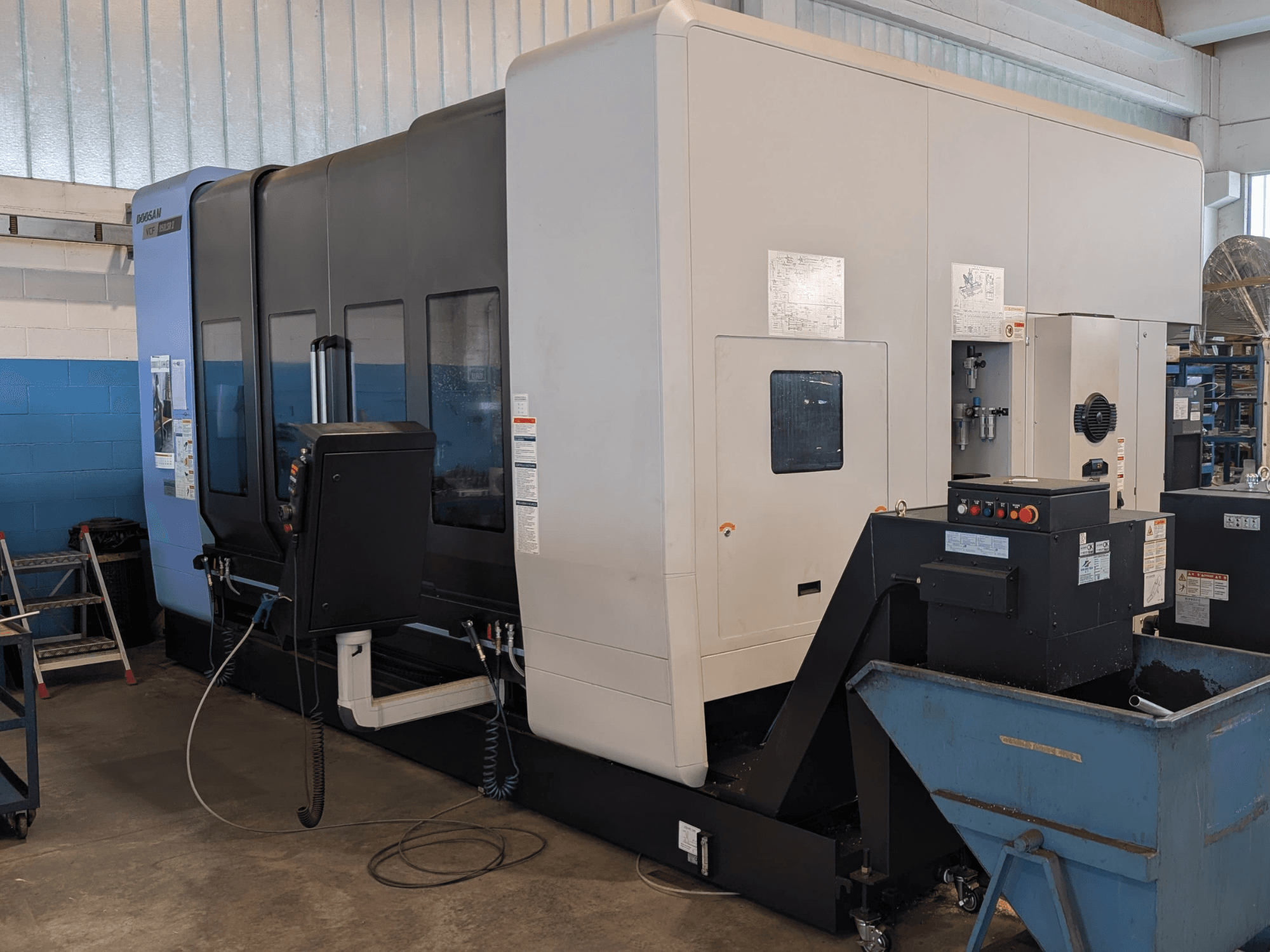 „DOOSAN VCF850LSR-II“ vertikalaus apdirbimo centro šoninis vaizdas, kuriame matomas valdymo pultas, aušinimo skysčio sistema ir tvirta konstrukcija.