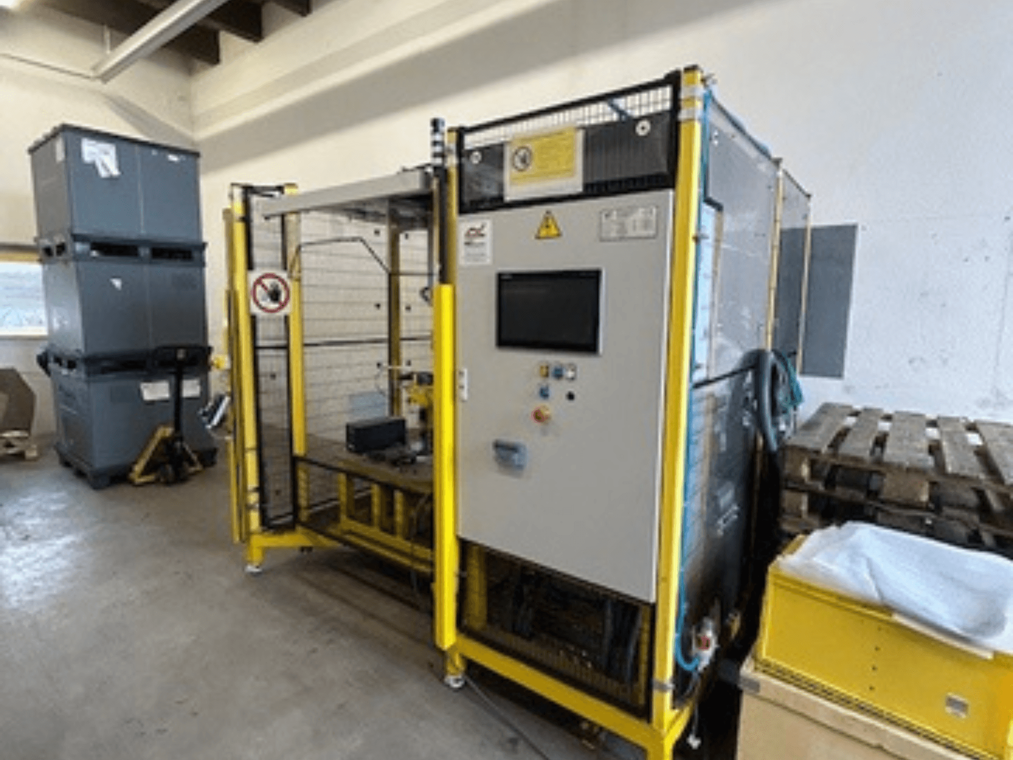 Pramoninė mašina su valdymo skydeliu ir saugos įtaisais, vaizdas iš priekio; geltonas rėmas, pilkos dėžės ir padėklai fone.