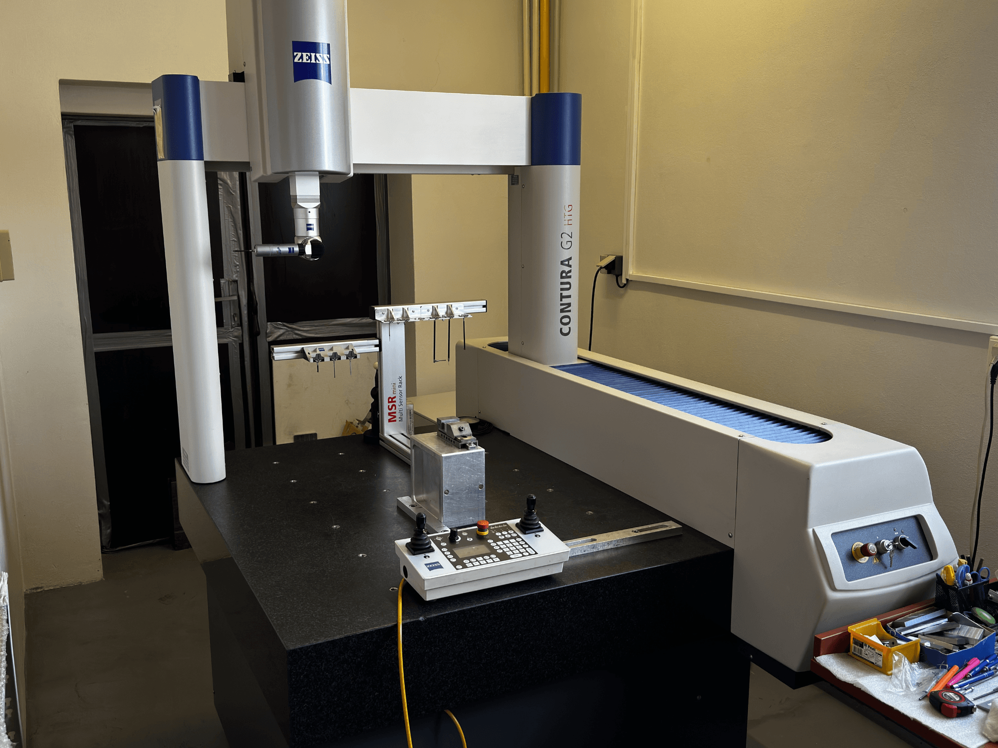 "ZEISS Contura G2" KMM laboratorijoje, priekinis vaizdas, kuriame matoma matavimo rankena, valdymo skydelis ir gretima darbo vieta.