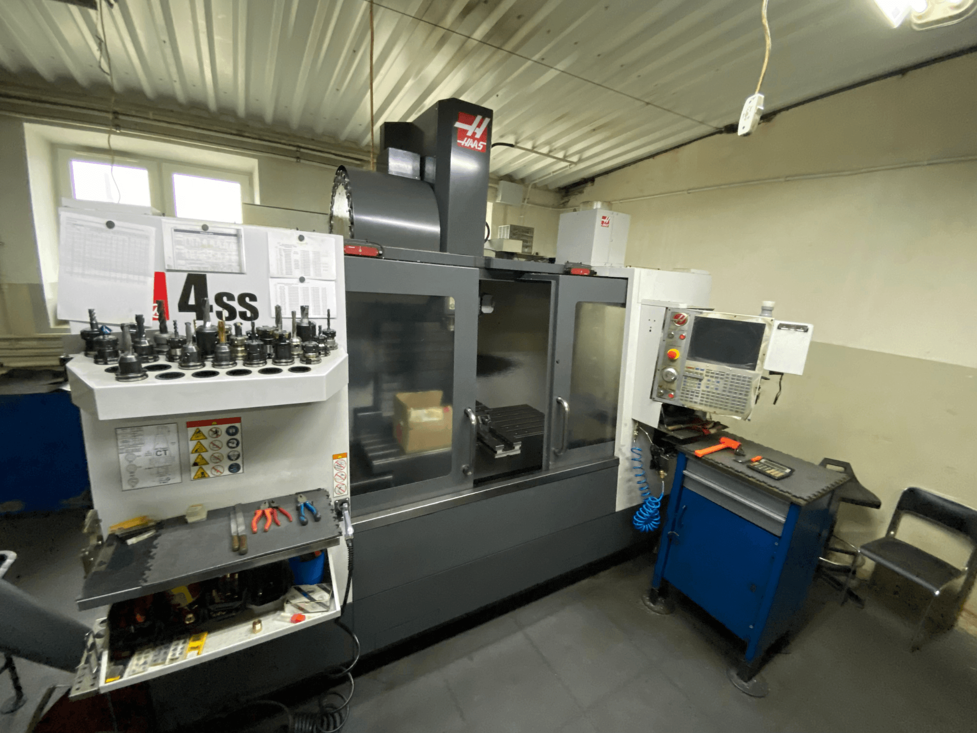Vertikalusis apdirbimo centras „Haas VF-4SS“, vaizdas iš priekio su įrankių laikikliais ir valdymo pultu. Matomi įrankiai ir darbo erdvė.