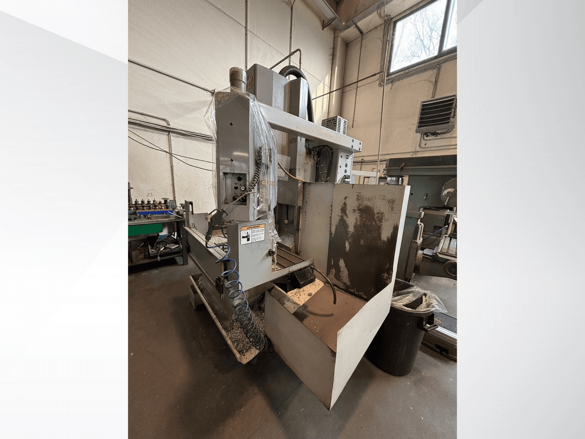 Vertikaliosios frezavimo staklės su apsauginiu dangčiu, vaizdas iš šono; matoma aušinimo skysčio žarna ir valdymo skydelis. Idealiai tinka apdirbti.