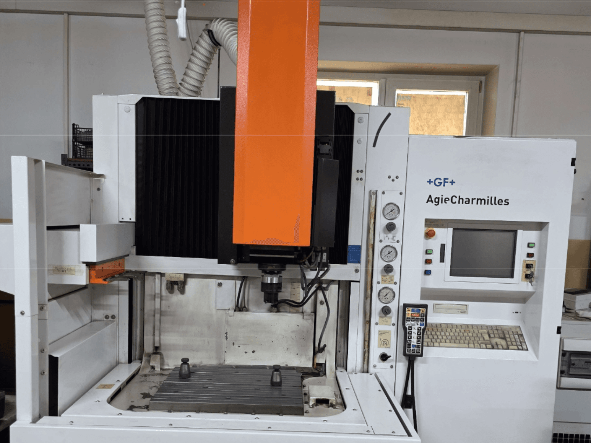 "AgieCharmilles" apdirbimo centras iš priekio su dideliu oranžiniu sukliu, valdymo pultu ir matomu darbo stalu.