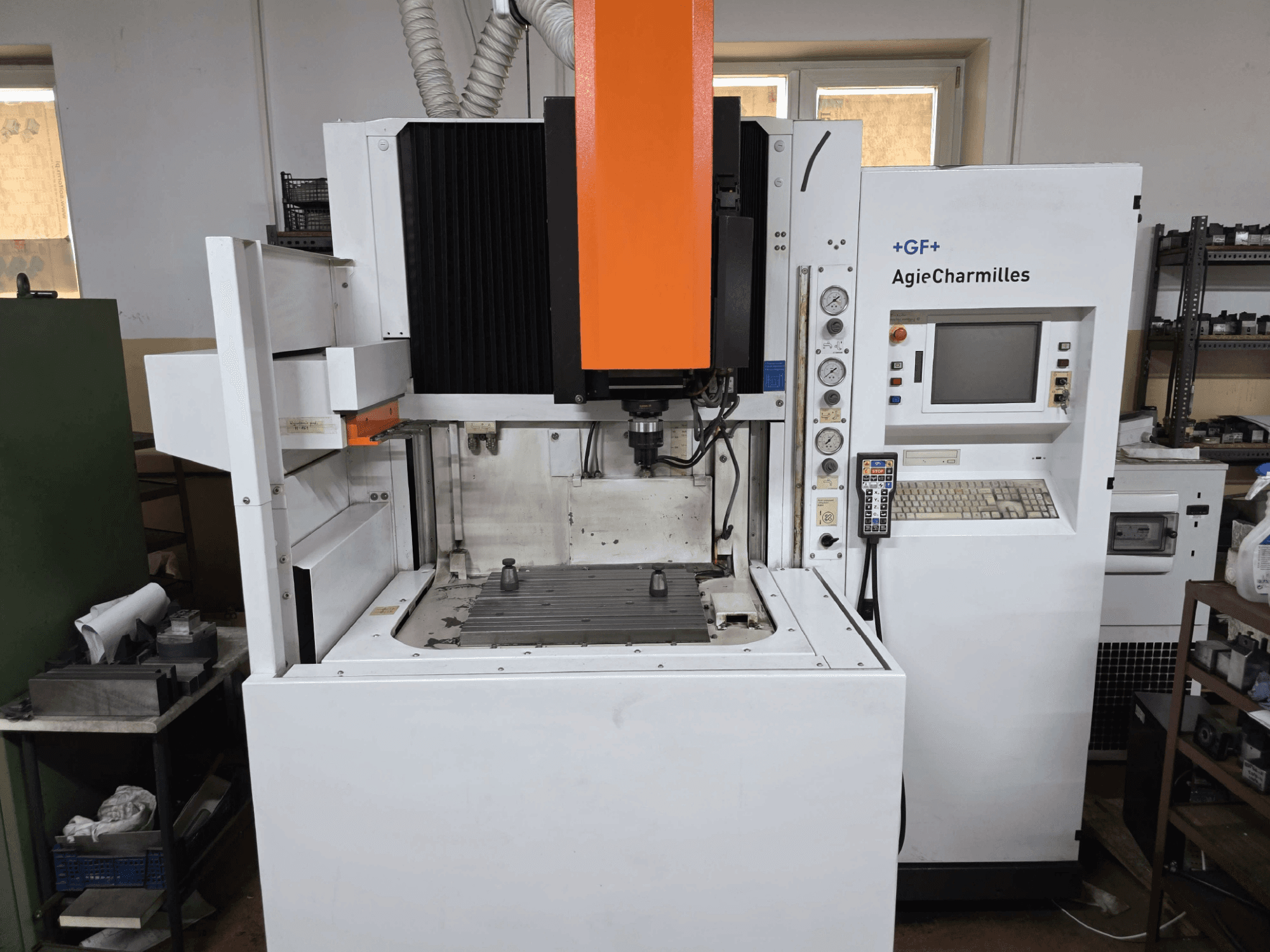 GF AgieCharmilles CNC staklės, vaizdas iš priekio su ryškiai matomu oranžiniu sukliu, skaitmeniniu valdymo pultu ir pritvirtintu gręžimo stalu.