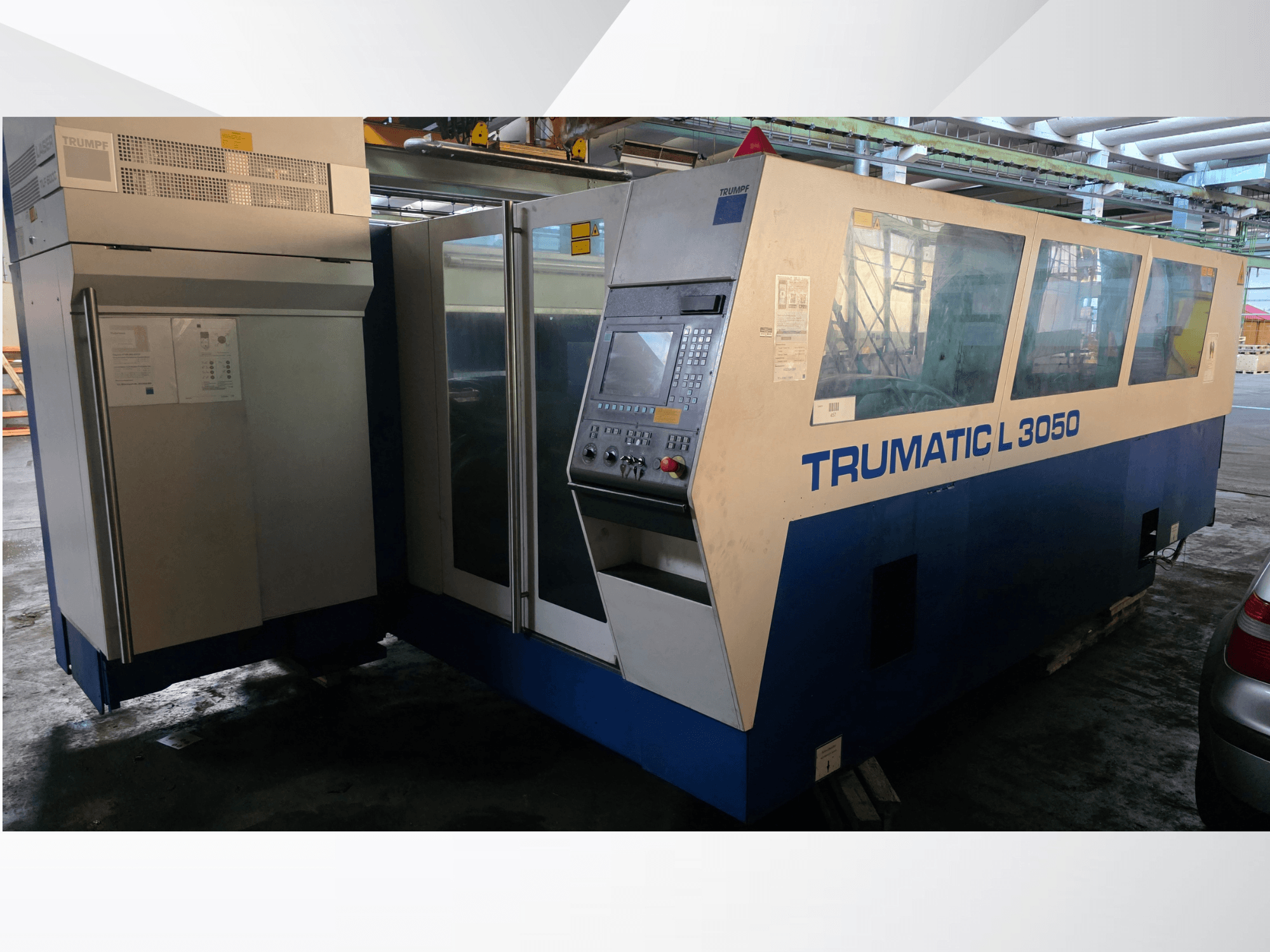 TRUMPF Trumatic L 3050 CO2 lazerinio pjovimo staklės, vaizdas iš priekio, su valdymo pultu ir dideliais stikliniais langais.