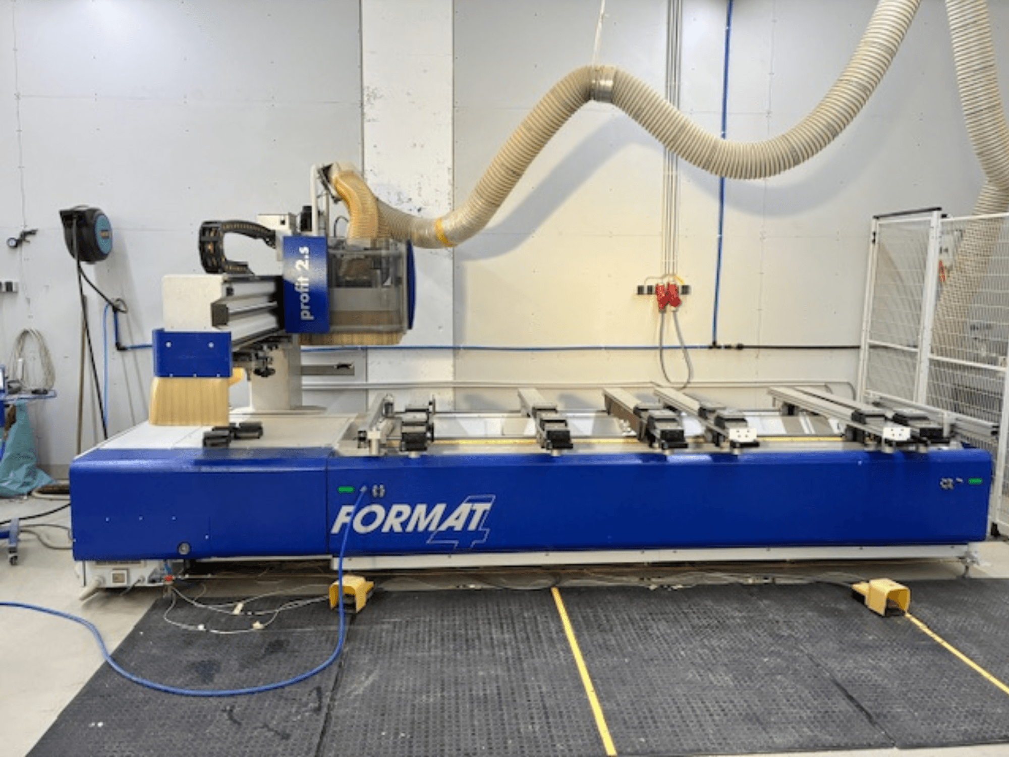 Mėlynas FORMAT 4 CNC maršrutizatorius, modelis Profit 2.5, šoninis vaizdas, rodantis pjovimo zoną ir dulkių ištraukimo sistemą, ant guminio kilimėlio.