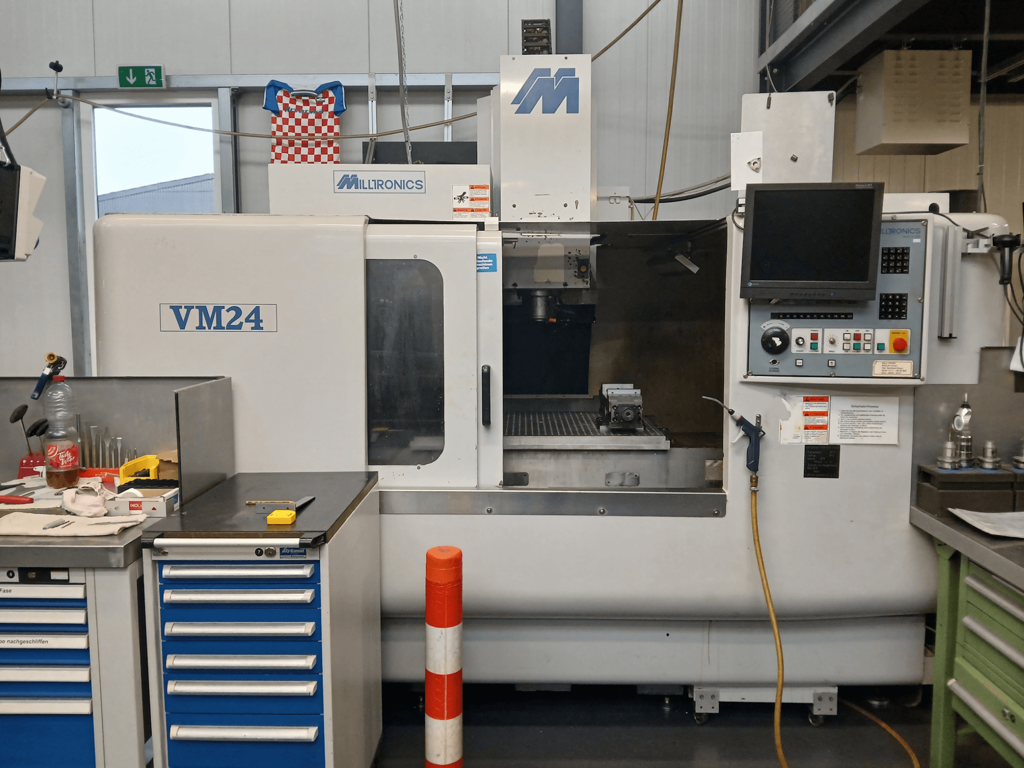 CNC frezavimo staklės "Milltronics VM24", parodytos iš priekio, su valdymo skydeliu, įrankių laikymo vieta ir darbo zonos sąranka.