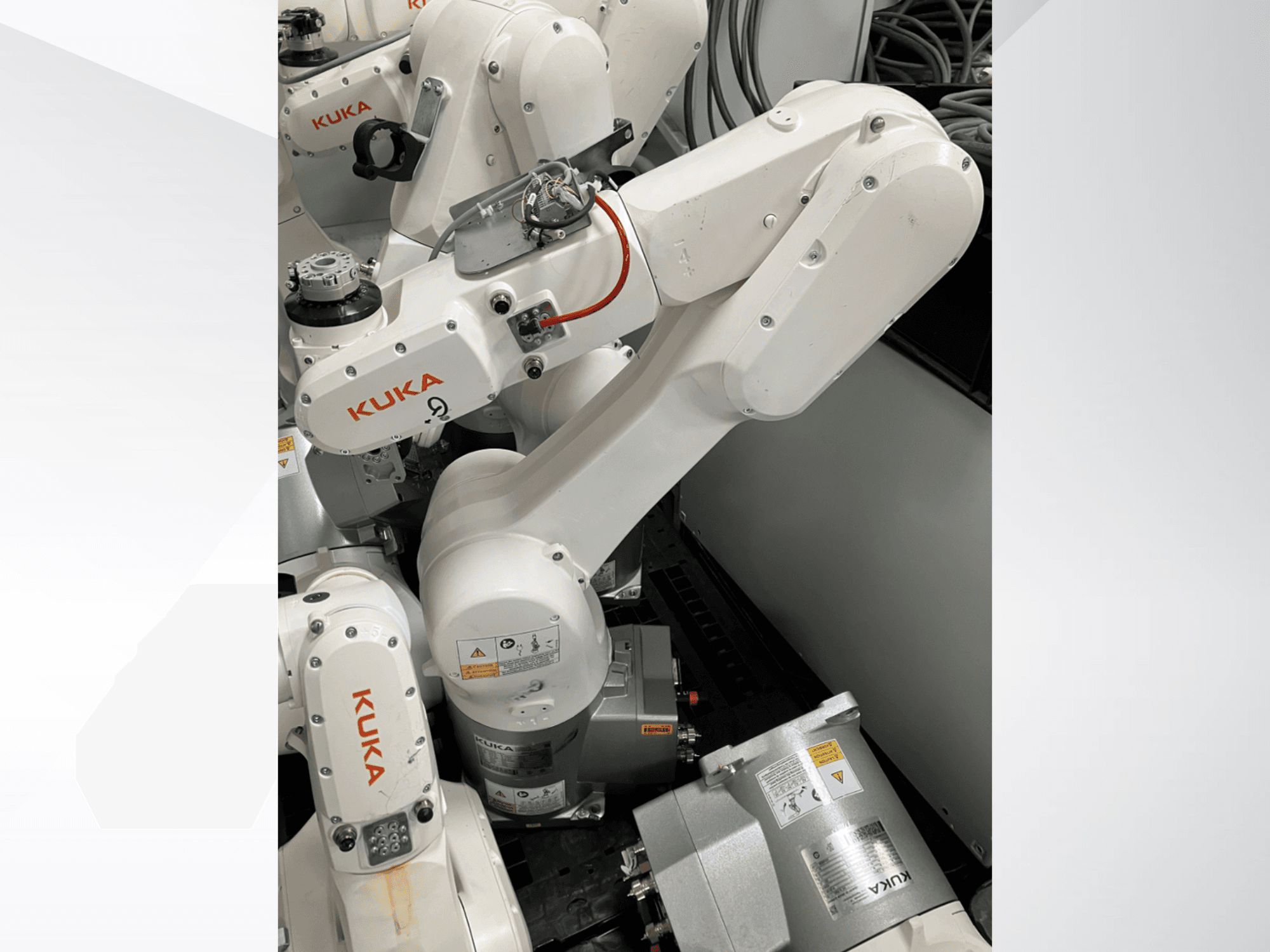 KUKA KR 6 R900 CR roboto rankos vaizdas iš šono; matomi varikliai ir jungtys, paženklinti saugos įspėjimais ir mechaninės rankos.