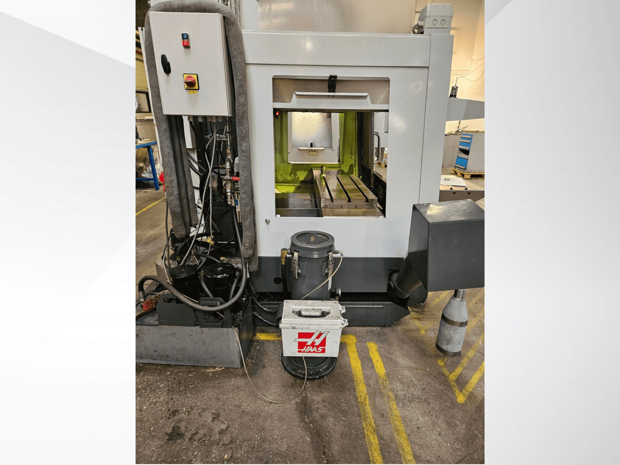 "Haas" CNC staklių priekinis vaizdas, kuriame matomas valdymo skydelis, aušinimo skysčio bakas ir apdirbta lova.