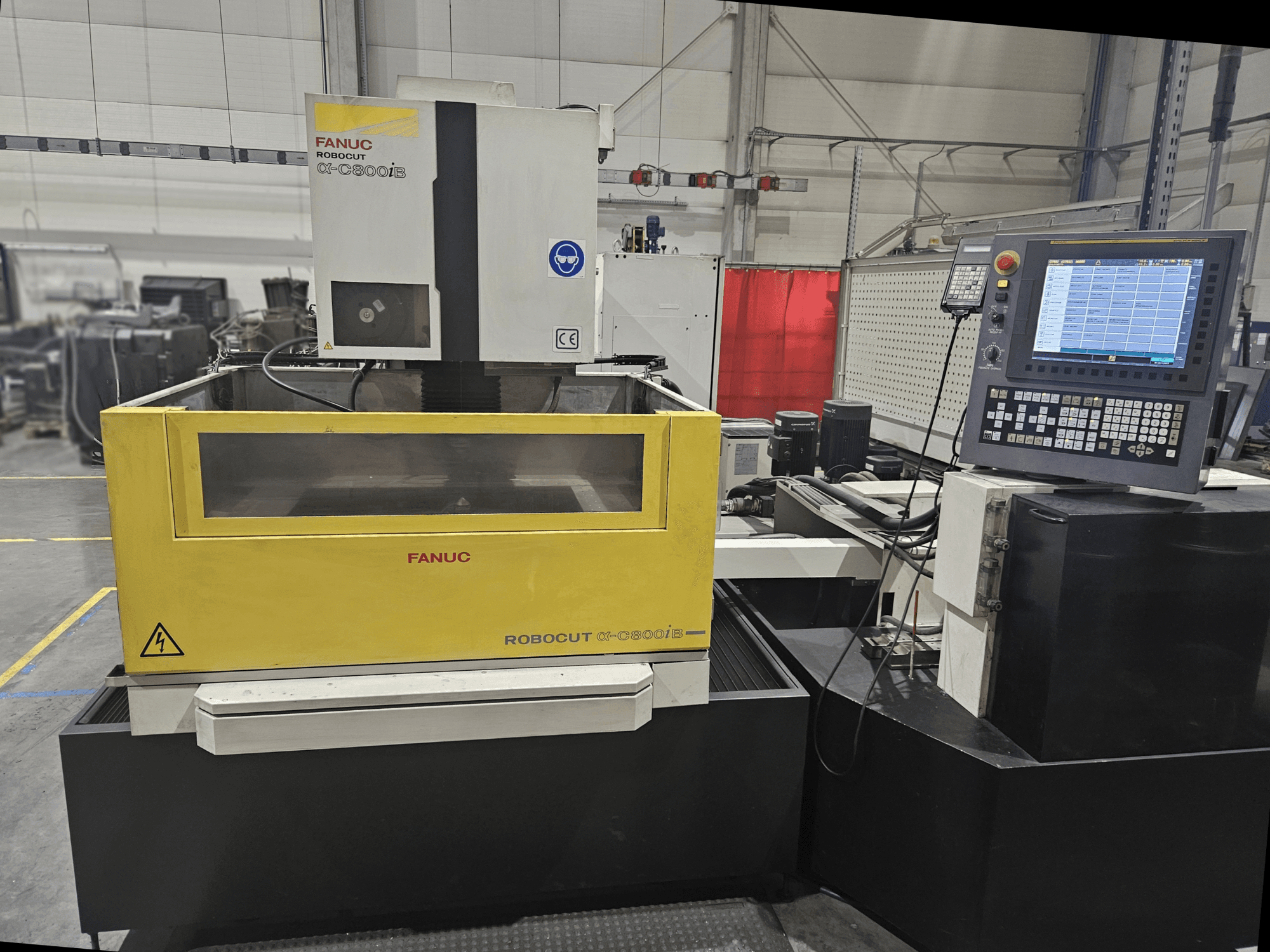 FANUC Robocut α-C600iB priekinis vaizdas su geltonos ir pilkos spalvos mašinos korpusu, CNC valdymo skydeliu ir darbiniu ekranu.