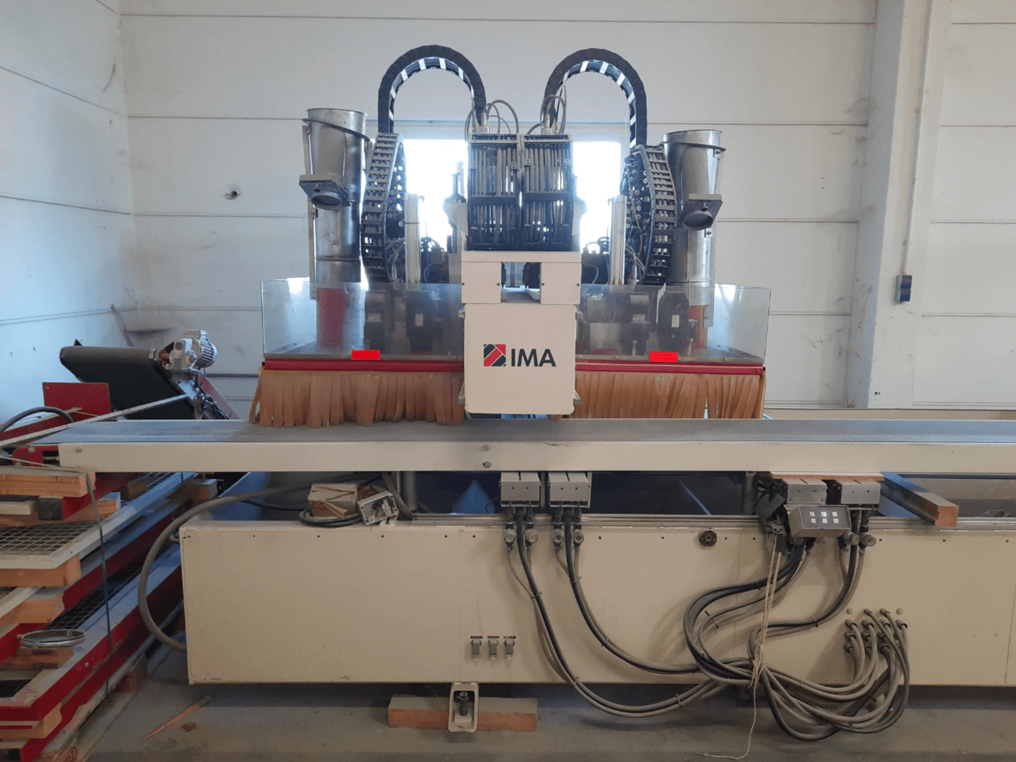 CNC medžio apdirbimo centras „IMA BIMA 610 V“, vaizduojamas iš priekio, su šepetėliais, valdymo elementais ir darbo stalu.