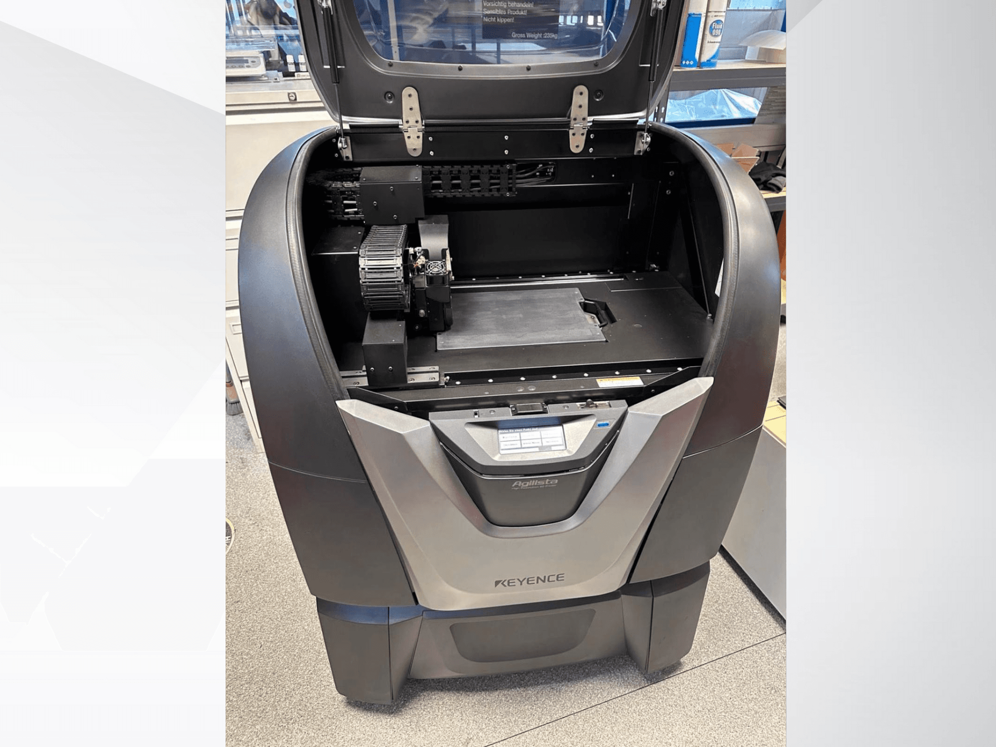 KEYENCE Agilista 3D spausdintuvo "Agilista" priekinis vaizdas, kuriame matomas atviras viršus, didelė surinkimo platforma ir vidiniai mechaniniai komponentai.