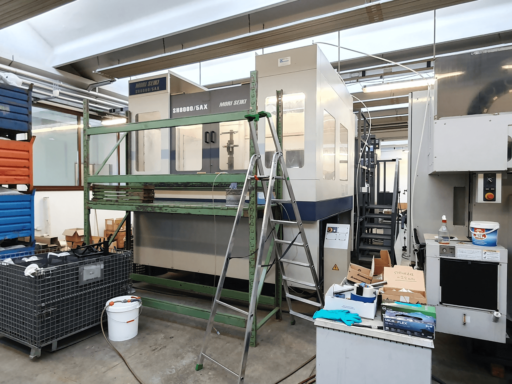 Mori Seiki SH-8000/5AX CNC staklės dirbtuvėse, vaizdas iš priekio, šalia - dirbtuvių įrankiai ir laikymo dėžės.