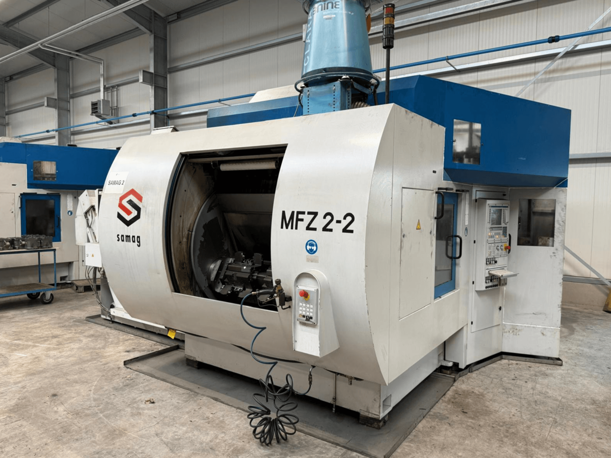 Samag MFZ 2-2 frezavimo staklės iš šono, matoma didelė atvira kamera ir valdymo skydelis su įvairiais mygtukais ir rankenėlėmis.