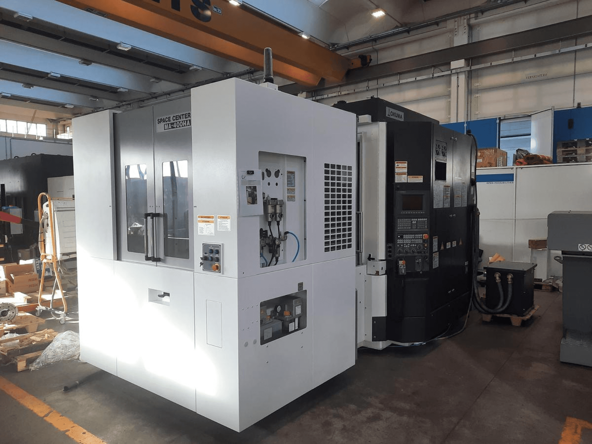 SPACE CENTER IM-400HAA ir OKUMA CNC staklių priekinis vaizdas, kuriame matomi įvairūs valdikliai ir gamintojo etiketės.