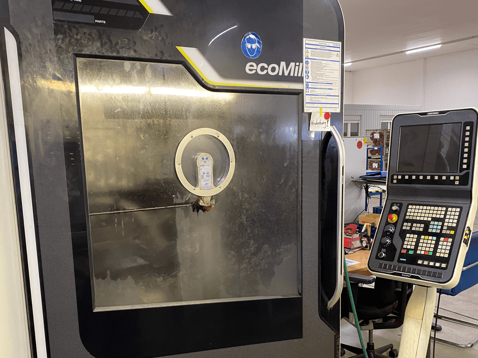 DMG MU 70 ECO frezavimo staklių vaizdas iš priekio: dešinėje matomas valdymo pultas, o pro stiklinį skydelį matomi vidiniai komponentai.