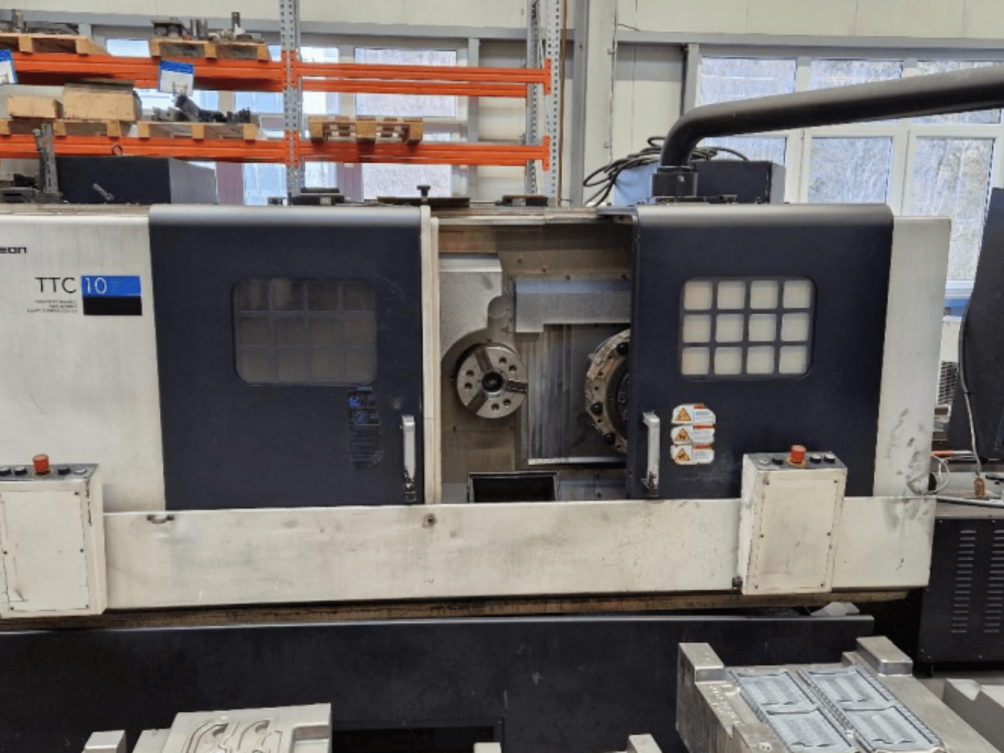 TTC 10 tekinimo staklių priekinis vaizdas, kuriame matyti valdymo skydelis, matomi griebtuvai ir darbo vieta su metalinėmis detalėmis.