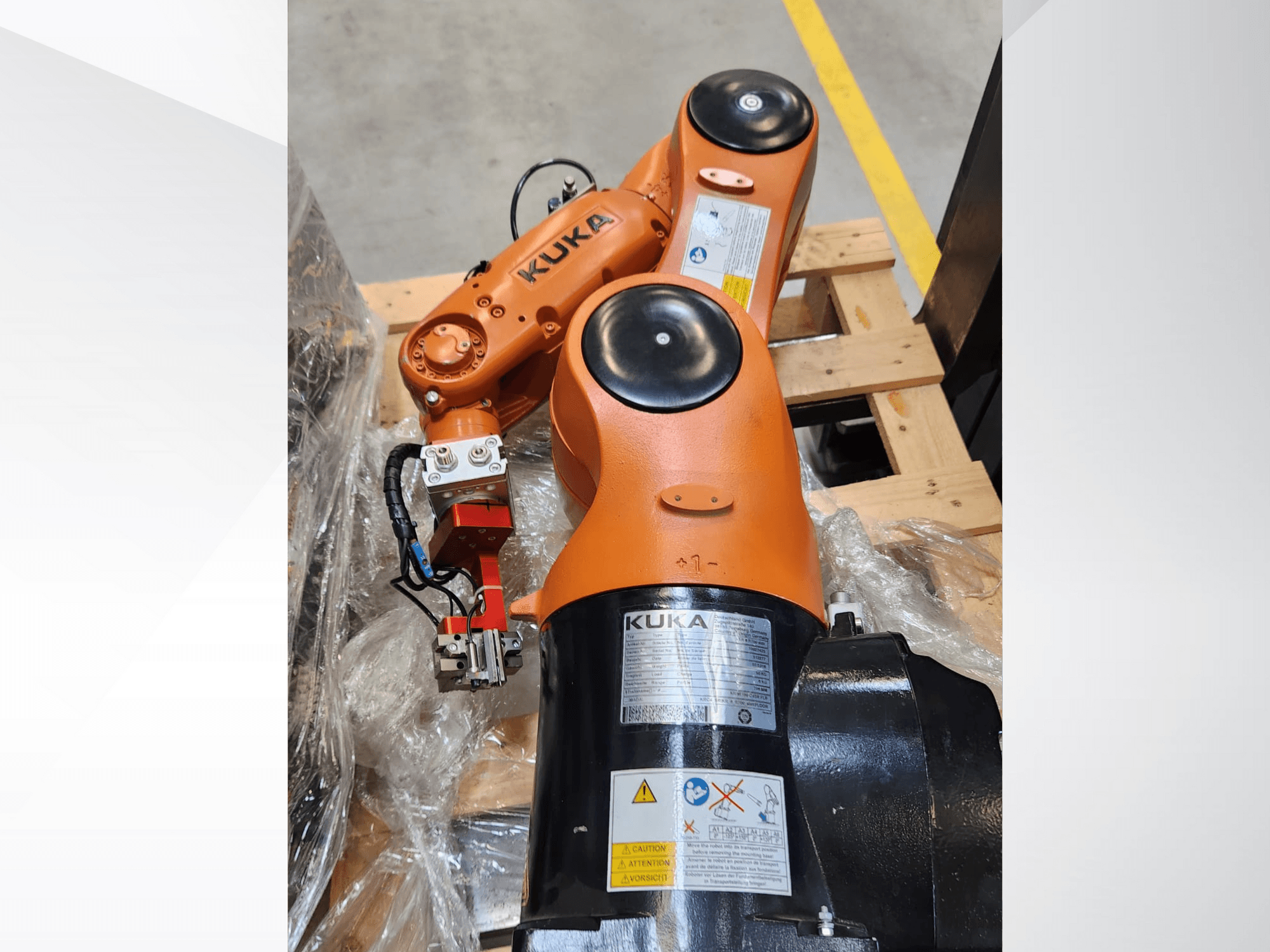 KUKA roboto rankos su oranžine apdaila, vaizdas iš šono, su griebtuvu ir valdymo laidais ant medinio padėklo.