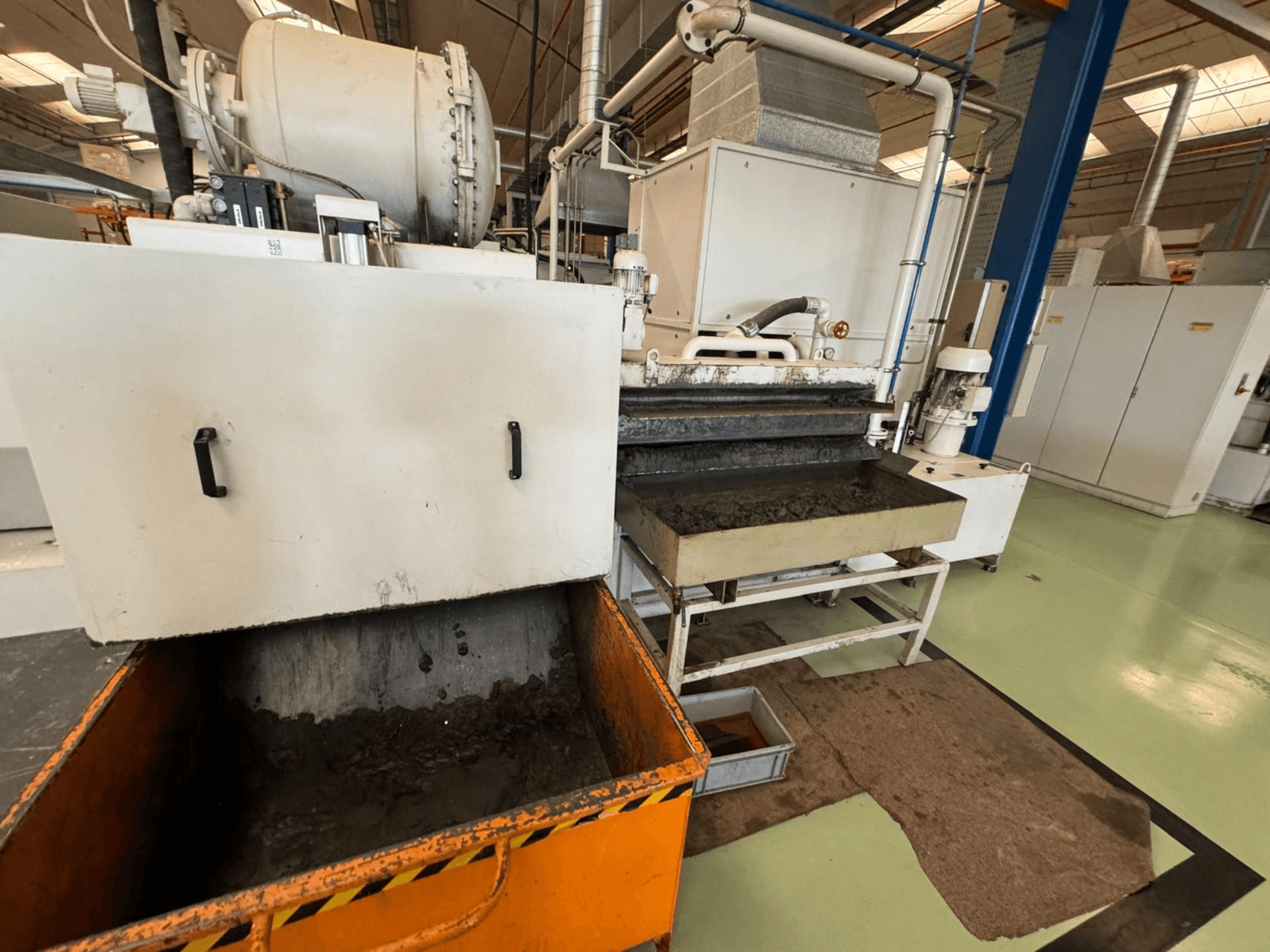 Pramonės perdirbimo įranga su oranžine atliekų dėže, vaizdas iš priekio; joje yra variklis, konvejeriai ir techninės priežiūros zona.