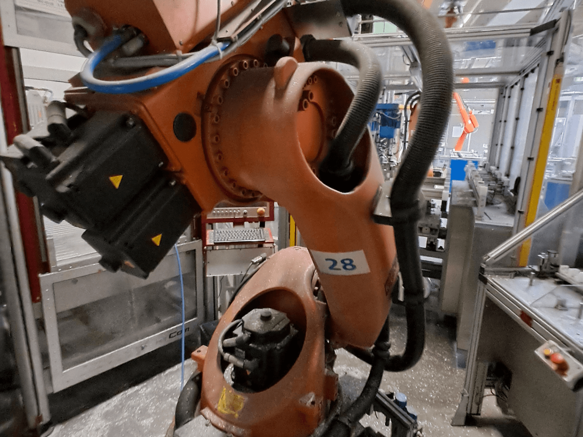 KUKA KR30-3 roboto rankos artimas vaizdas: oranžinis korpusas, pažymėtas numeriu 28, iš šono matomi varikliai ir laidai.