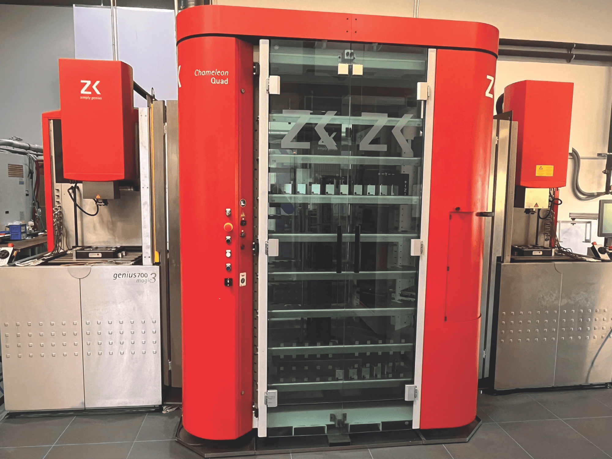 "ZK Chameleon Quad", vaizdas iš priekio, raudona išorė, stiklinės lentynos ir šalia esantis "Genius 700 Magic 3" įrenginys su valdymo pultu.