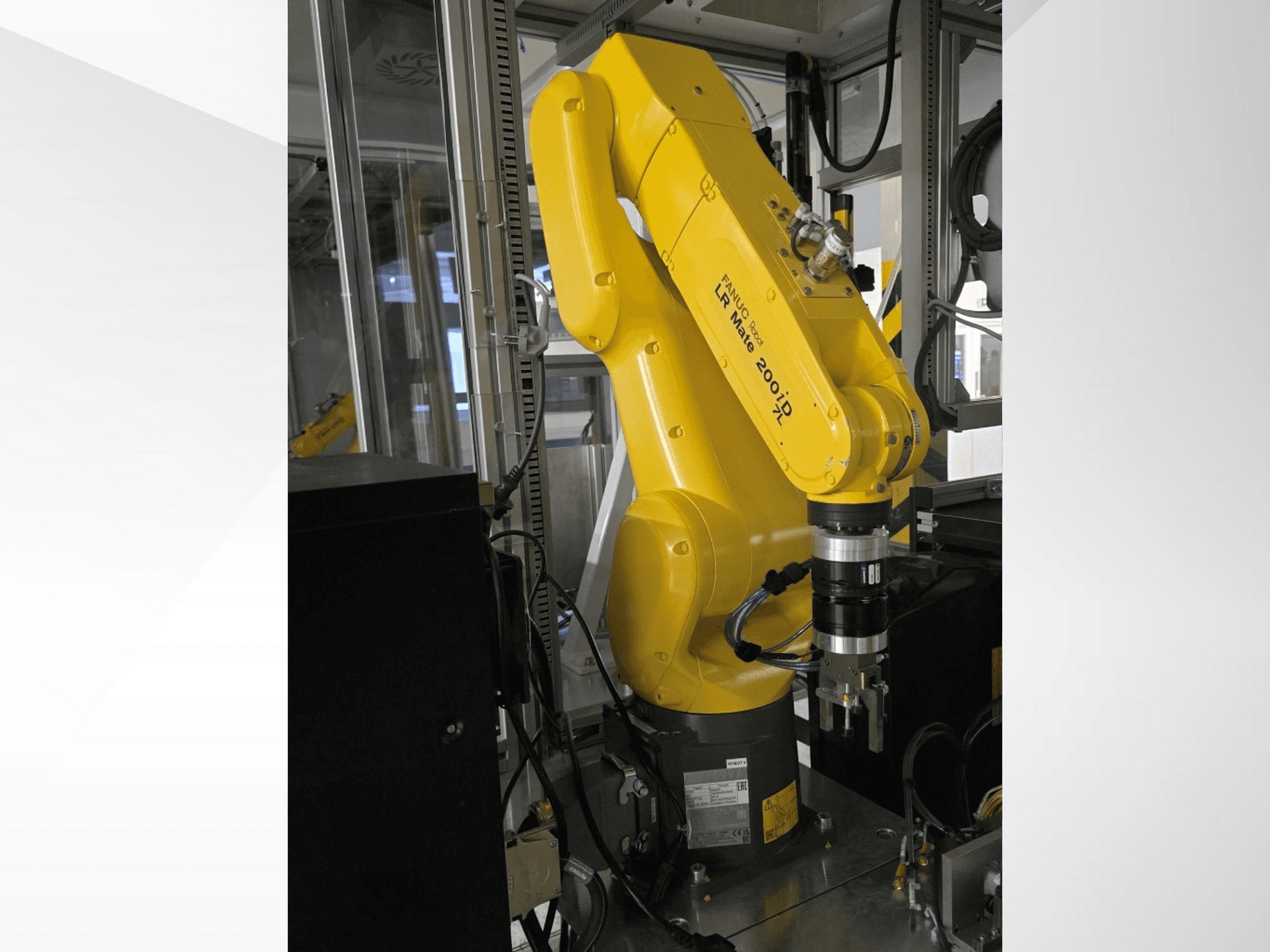 Geltonos spalvos "Fanuc LR Mate 200iD" roboto ranka, parodyta iš šono, su griebtuvu ir pritvirtintais įvairiais kabeliais.