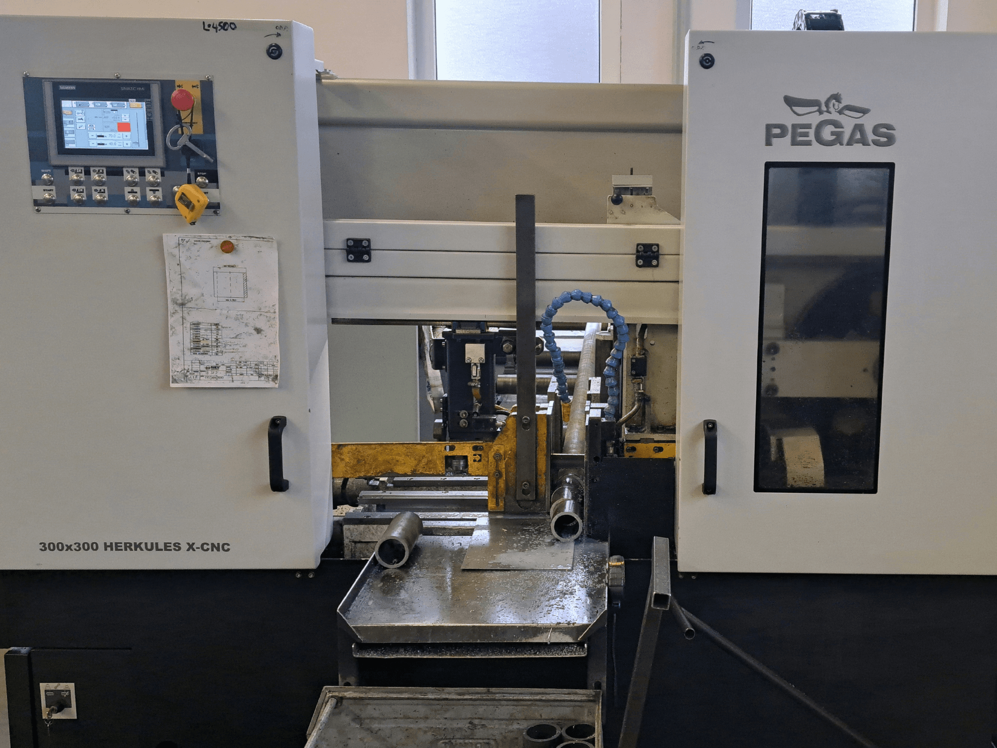 „Pegas HERKULES X-CNC 300x300“ lakštinio metalo apdirbimo staklės, vaizdas iš priekio, kuriame matomas valdymo pultas ir darbo zona su metalo detalėmis.