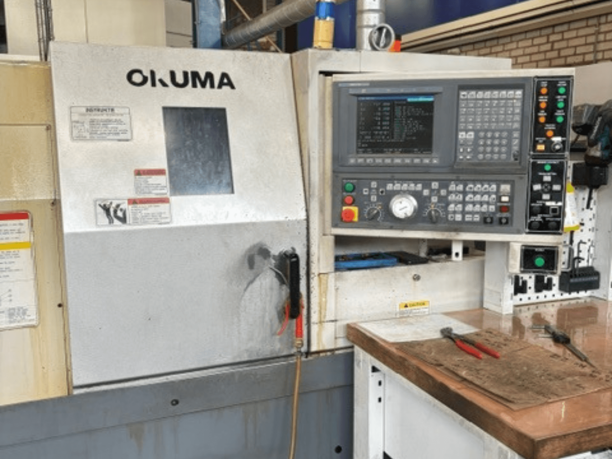 „Okuma ES-L10II“ horizontalaus tekinimo staklių vaizdas iš priekio, kuriame matomas valdymo skydas, ekranas ir darbo zona su įrankiais.