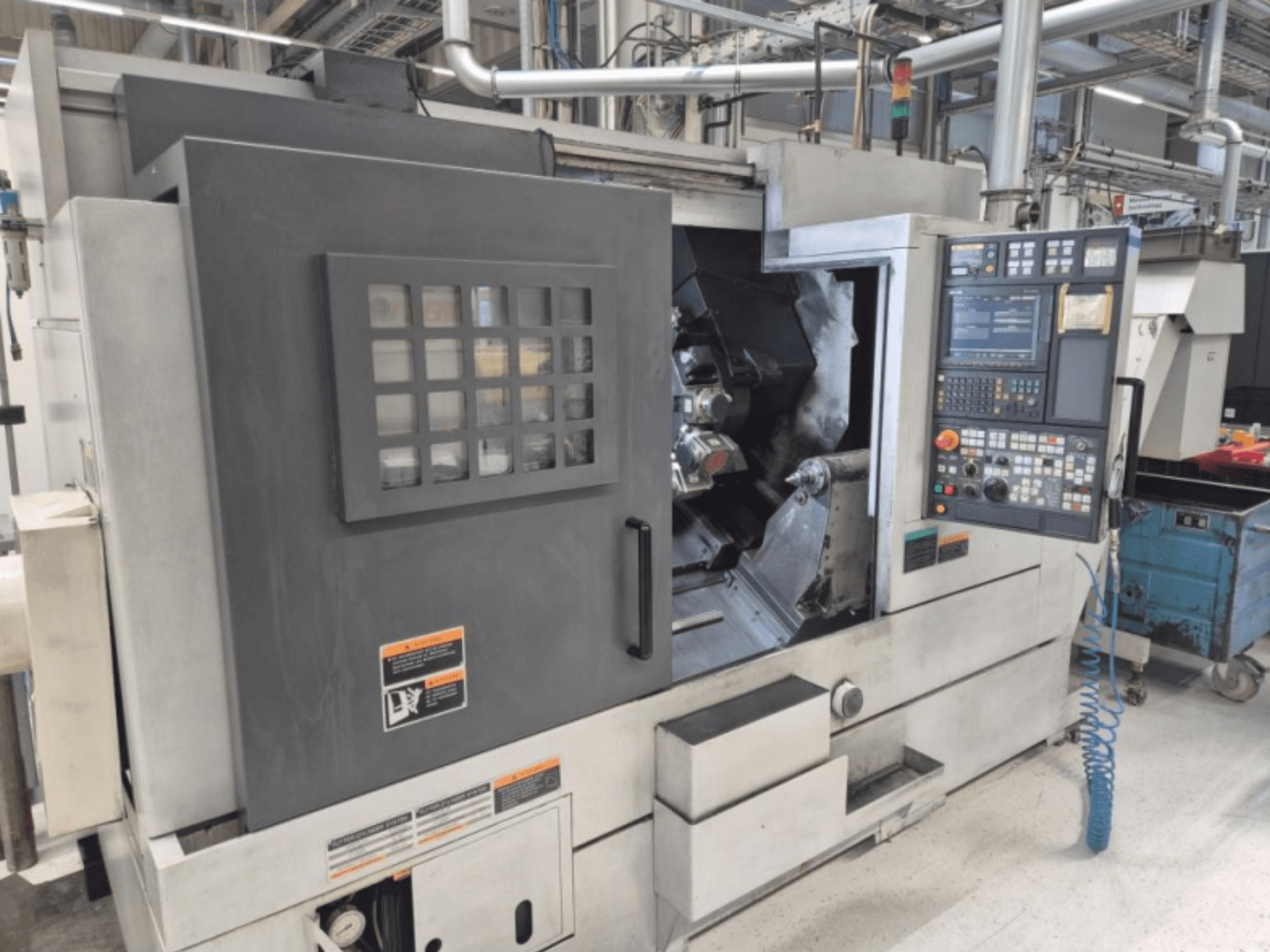 CNC tekinimo staklės su valdymo pultu, vaizdas iš priekio. Matoma darbo zona ir apsauginis langelis, prekės ženklas nežinomas.