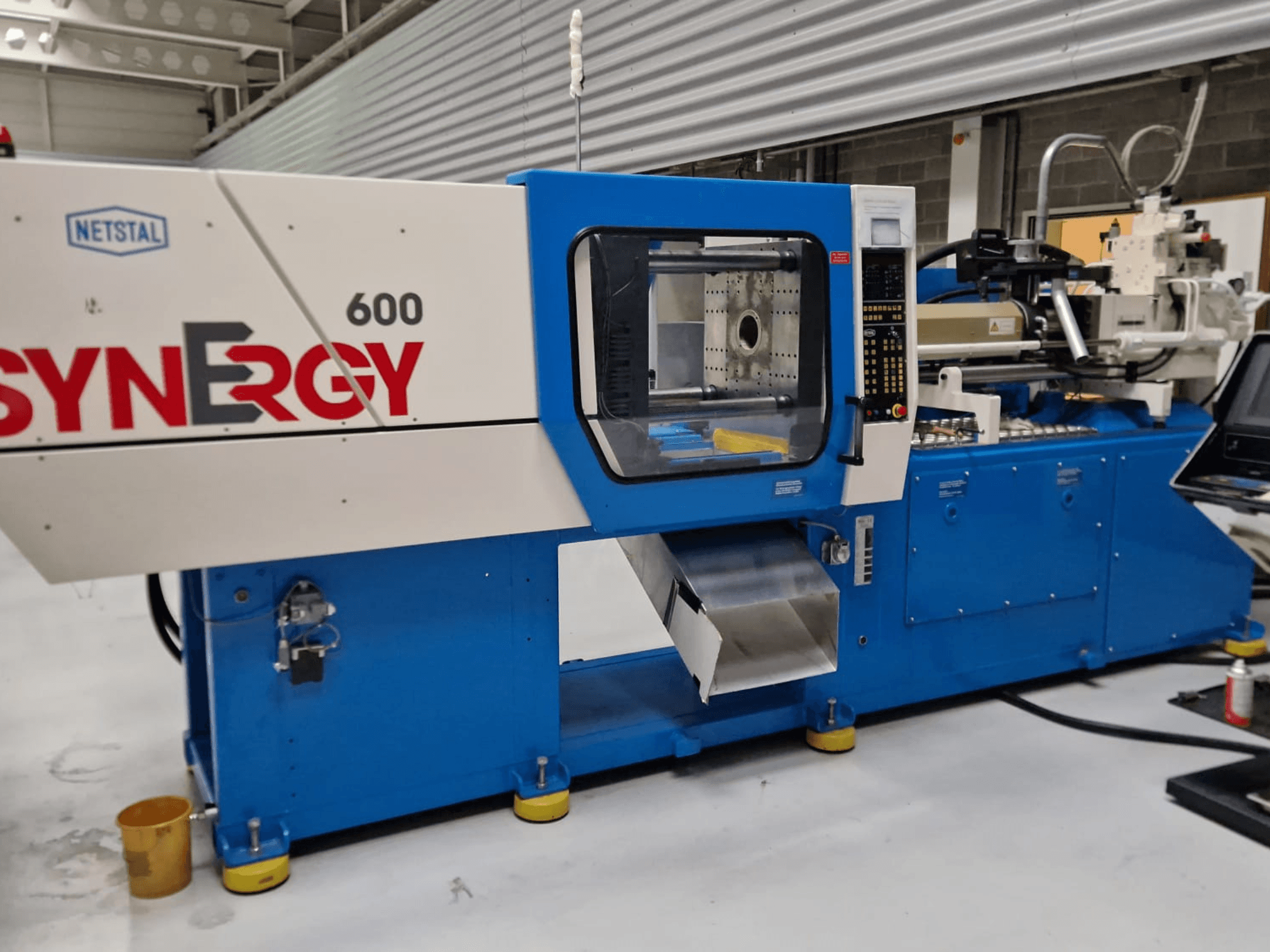 Netstal Synergy 600-230 hidraulinė įpurškimo mašina, šoninis vaizdas, kuriame matomas valdymo skydelis ir įpurškimo zona.