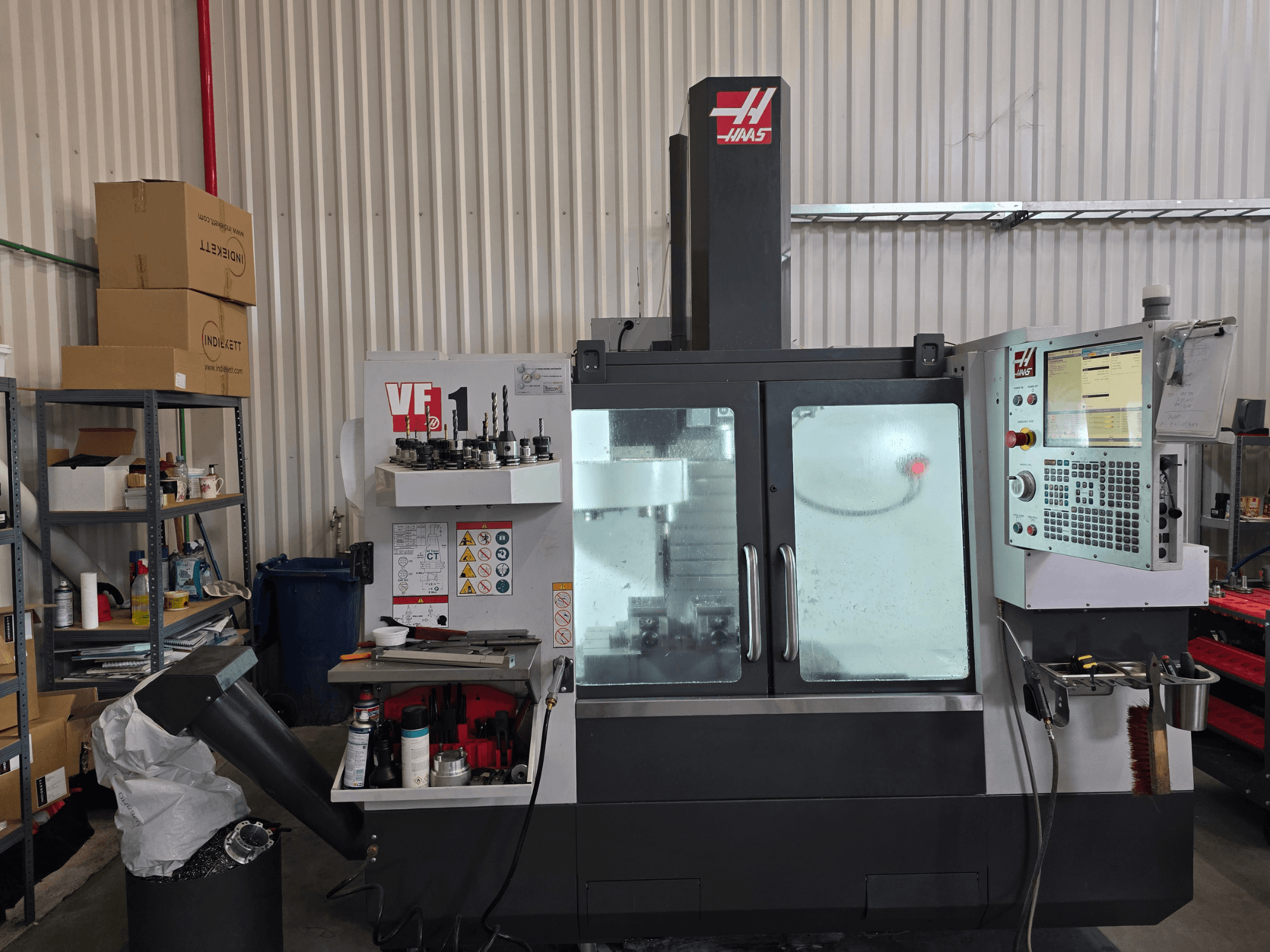 HAAS VF 1 vertikalusis apdirbimo centras dirbtuvėse, iš priekio matomas valdymo skydelis ir frezavimo zona su įrankiais.