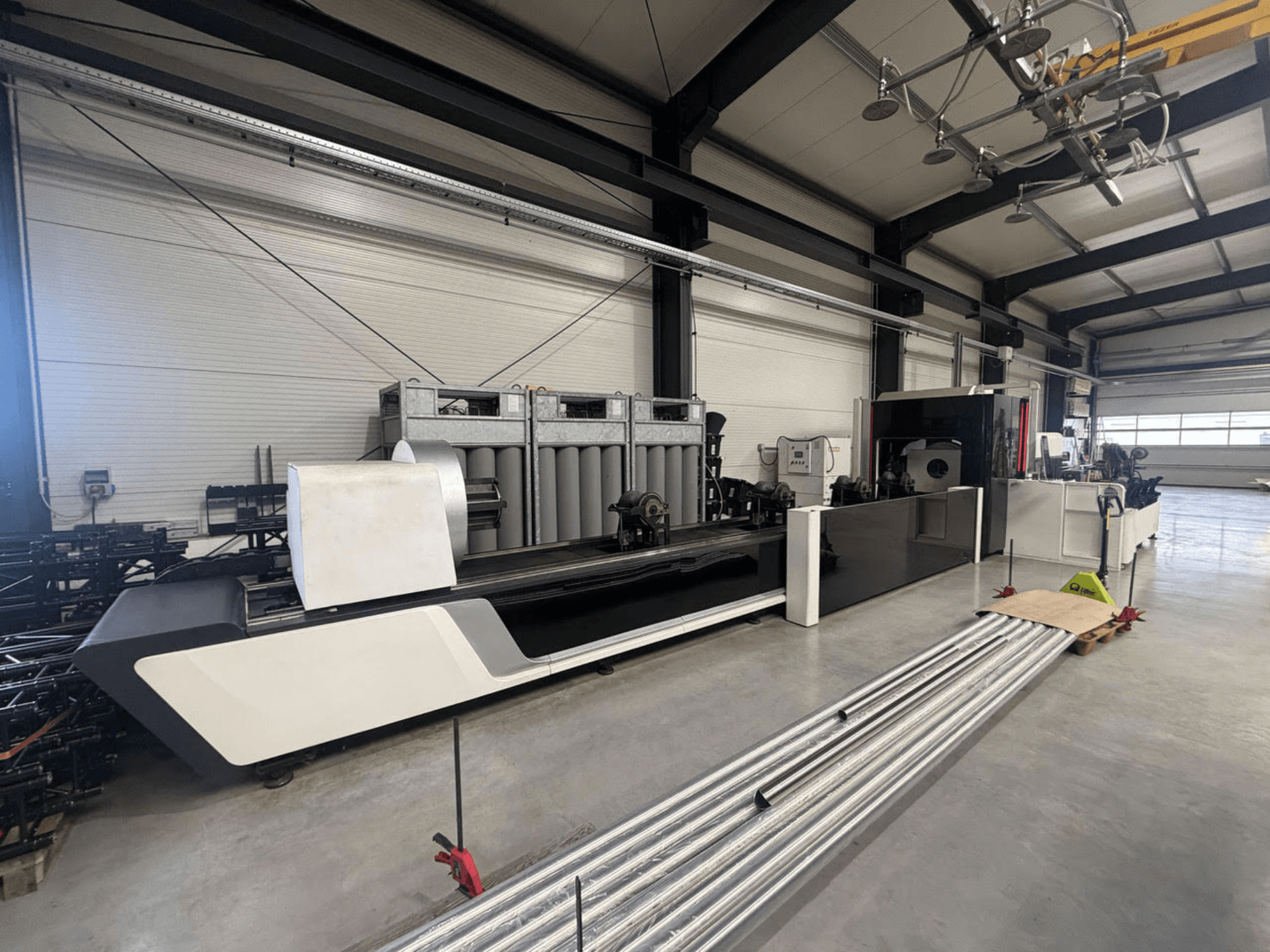 „Bodor X2260“ vamzdžių pjaustymo staklės dirbtuvėse; šoninis vaizdas, kuriame matomas staklių korpusas ir ant grindų gulintys metaliniai vamzdžiai.