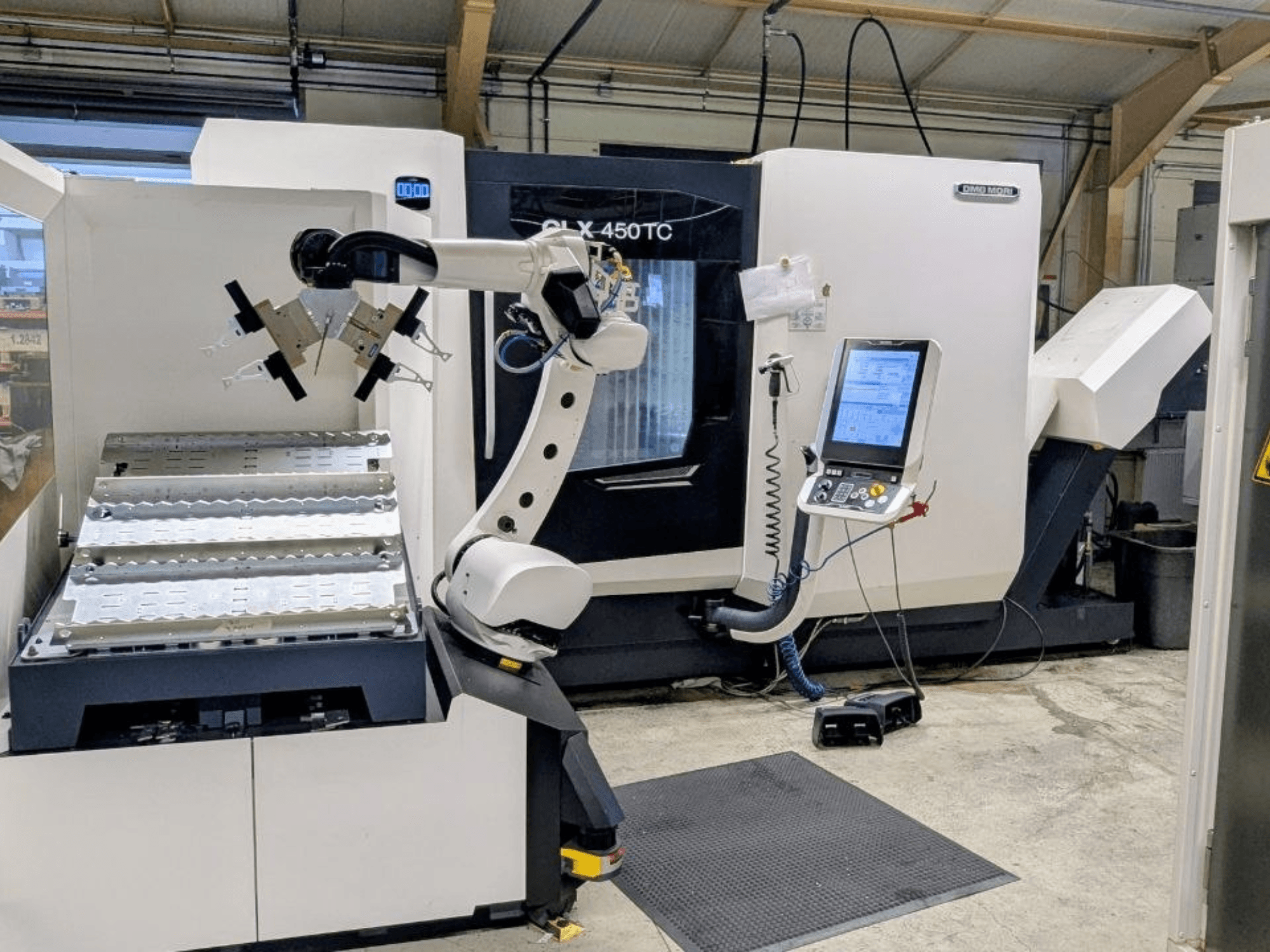 DMG MORI CLX 450 TC su „Robo2go“ sistema, vaizdas iš priekio, kuriame matoma robotinė ranka ir valdymo pultas šalia staklių.