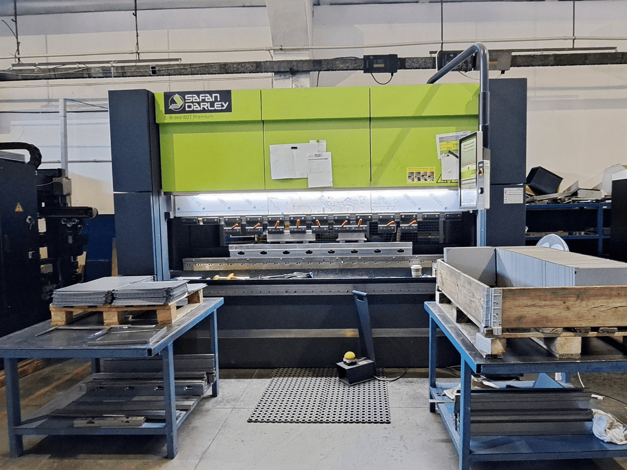 SAFAN E-Brake Premium 80-2550 presinis lenkimo staklės dirbtuvėse, vaizdas iš priekio, kuriame matomi sukrauti metaliniai lakštai ir valdymo pultas.