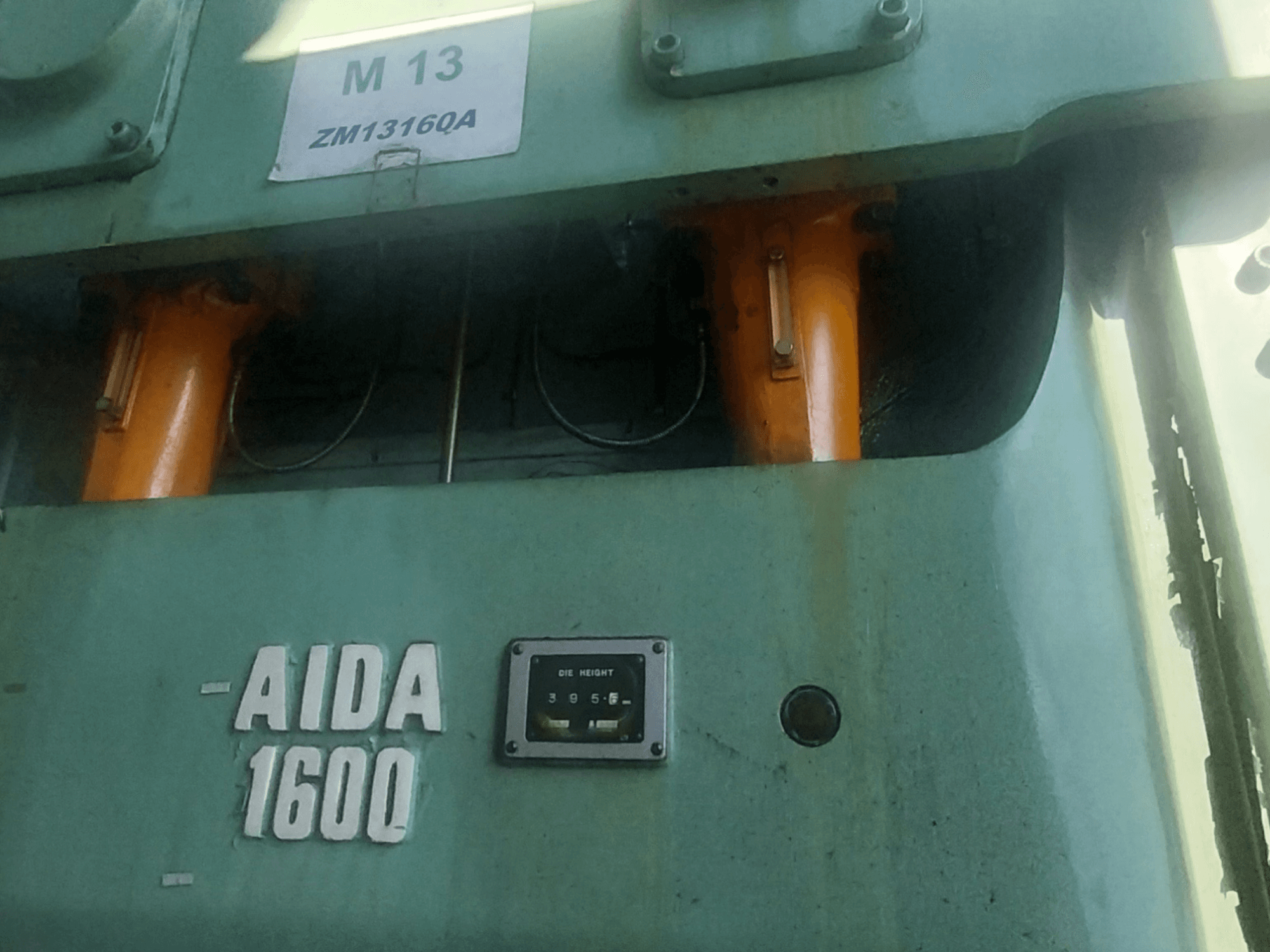 Mechaninis štampavimo presas AIDA NC2-1600, vaizdas iš priekio; matomi oranžiniai hidrauliniai komponentai ir štampų aukščio matuoklis.