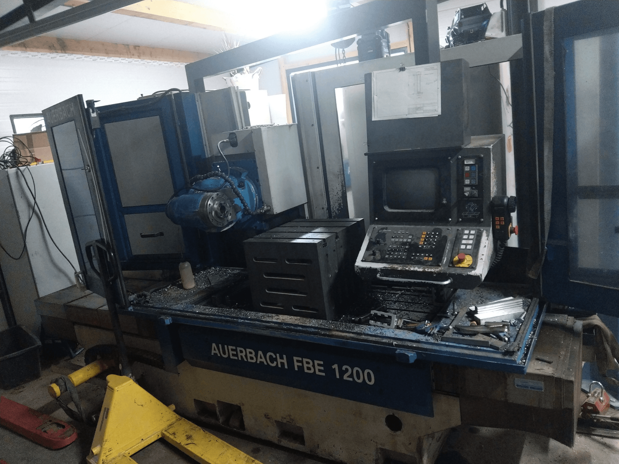 Auerbach FBE 1200 metalo gręžimo staklės, priekinis vaizdas, kuriame matyti valdymo skydelis, variklis ir metalo drožlės ant darbinio paviršiaus.