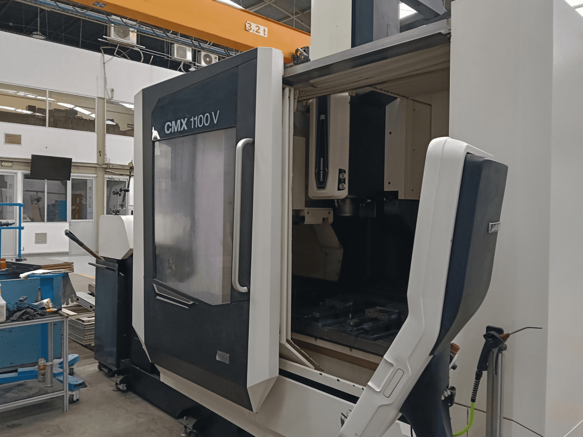 Vertikalusis apdirbimo centras „DMG MORI CMX 1100 V“ – vaizdas iš priekio, kuriame matomos atidarytos durys ir viduje esanti įrankių konfigūracija pramoninėje patalpoje.