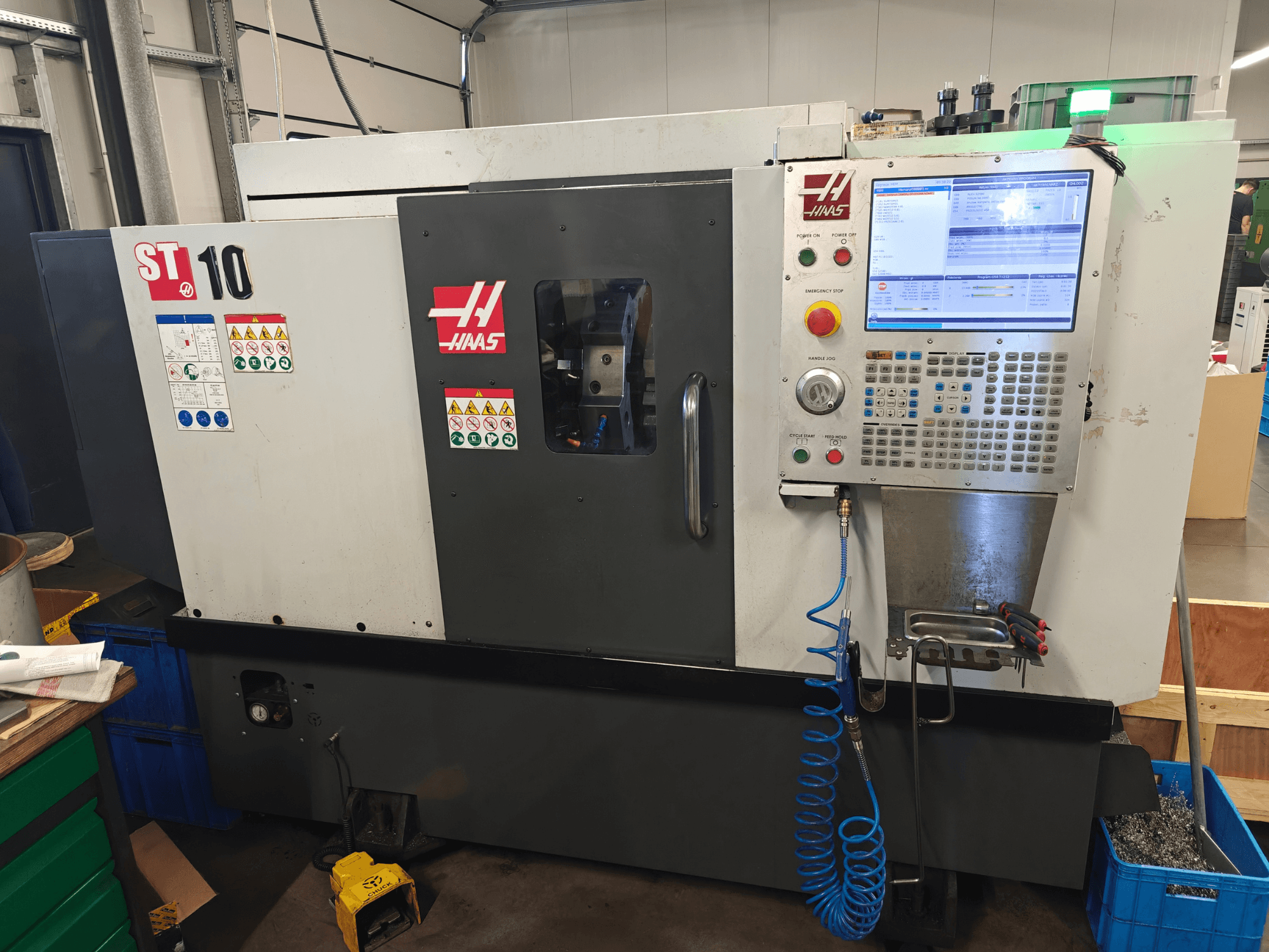 „Haas ST-10“ horizontalusis tekinimo staklės, vaizdas iš priekio, kuriame matomas valdymo skydas, saugos etiketės ir staklių konstrukcija.