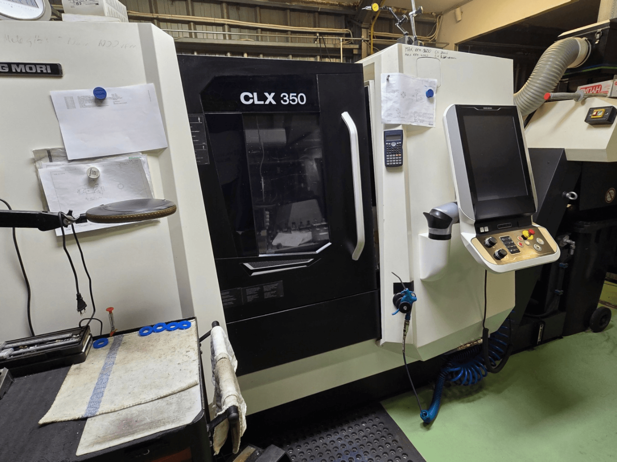 DMG MORI CLX 350 CNC tekinimo staklės dirbtuvėse; vaizdas iš priekio, matomas valdymo skydelis, įrankiai ir darbo vieta.