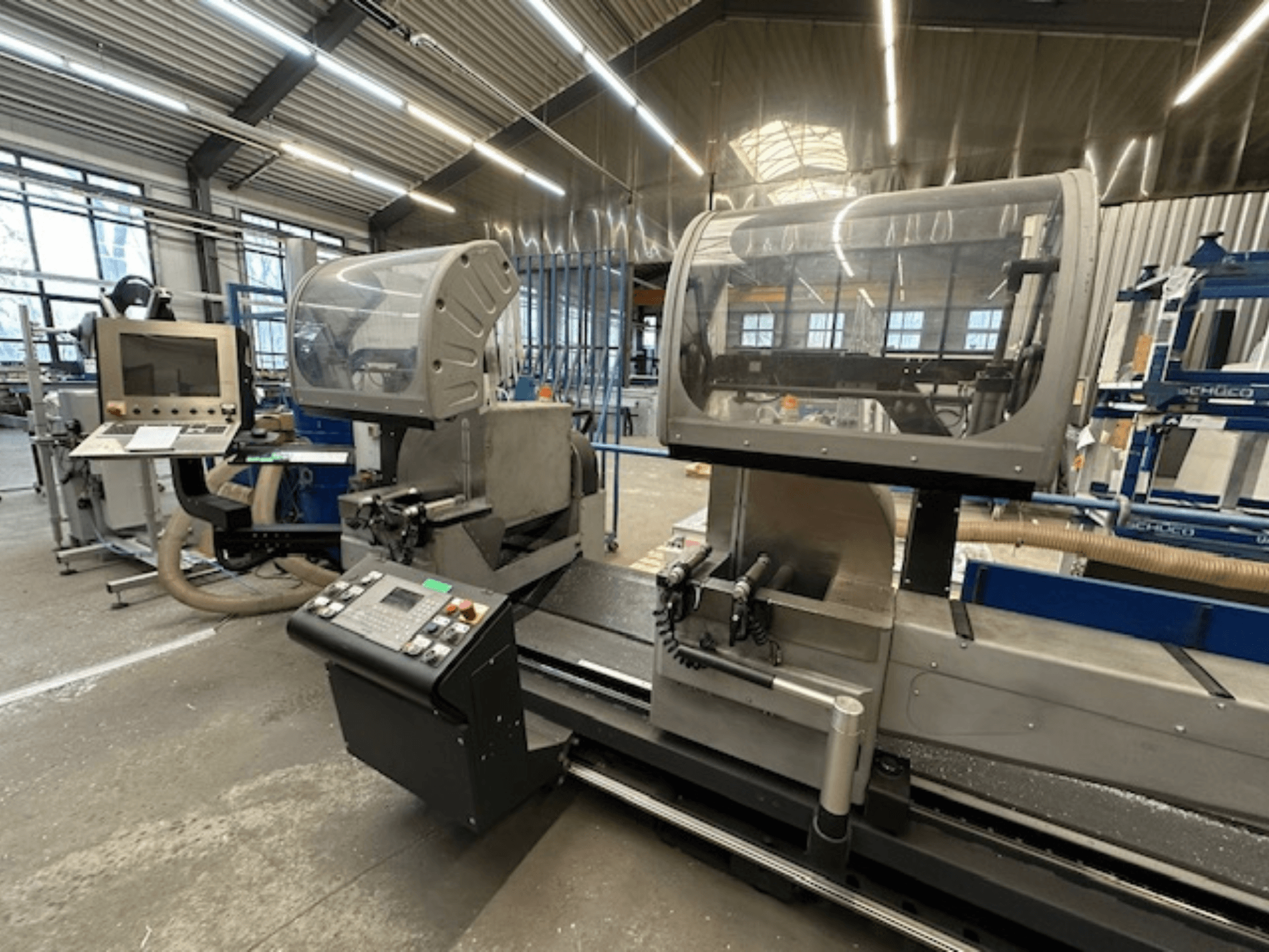 Diskinis metalo pjūklas SCHÜCO PDG E CUT, vaizdas iš priekio, su valdymo pultu, apsauginiais dangčiais ir pjovimo zona dirbtuvėse.